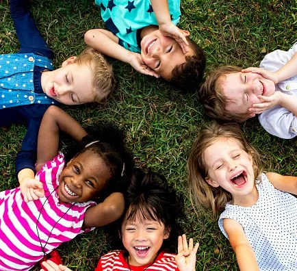 Groupe d'enfants souriants allongés en cercle sur l'herbe.