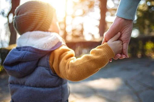 Une personne adulte tenant la main d'un enfant dans un parc lors d'une journée ensoleillée.