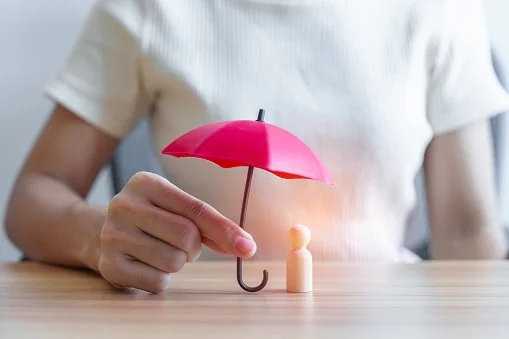 Main tenant un petit parapluie rose au-dessus d'une figurine debout sur une table en bois