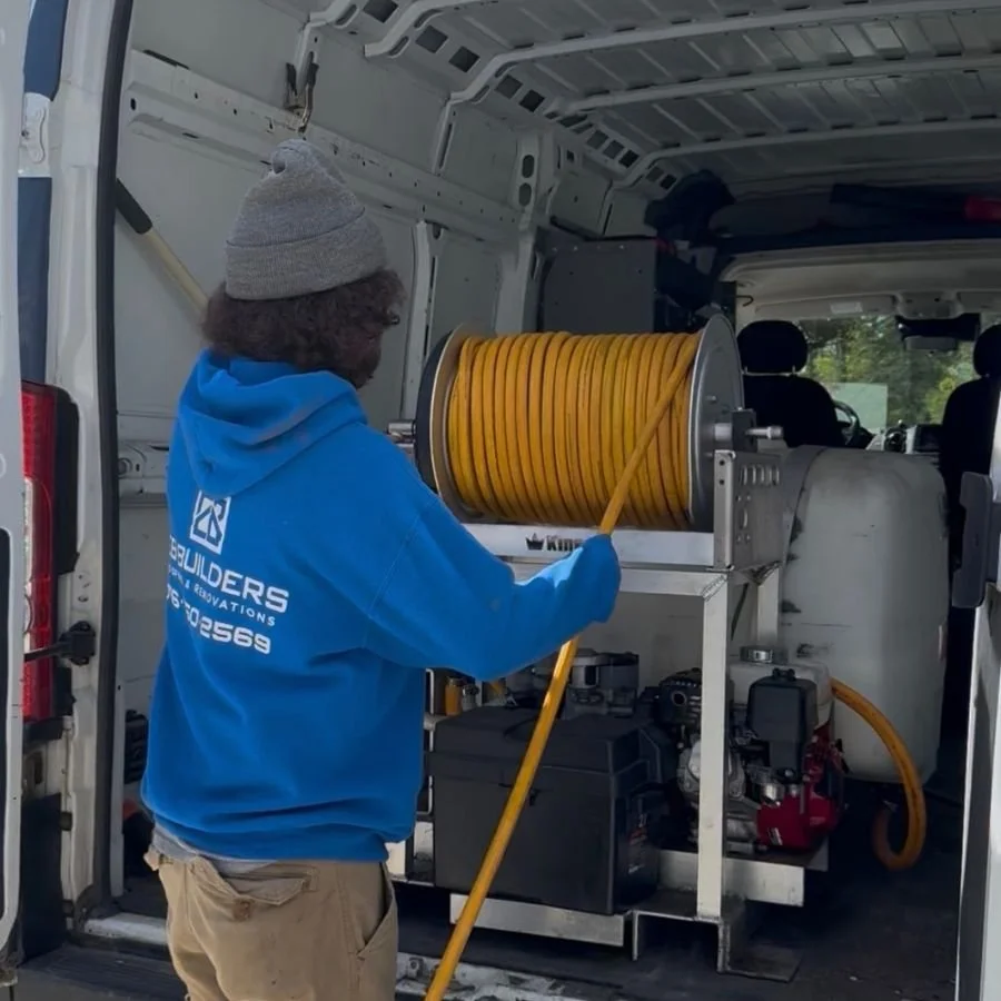 A man in a gray beanie and blue hoodie operating a yellow hose reel inside a work van.