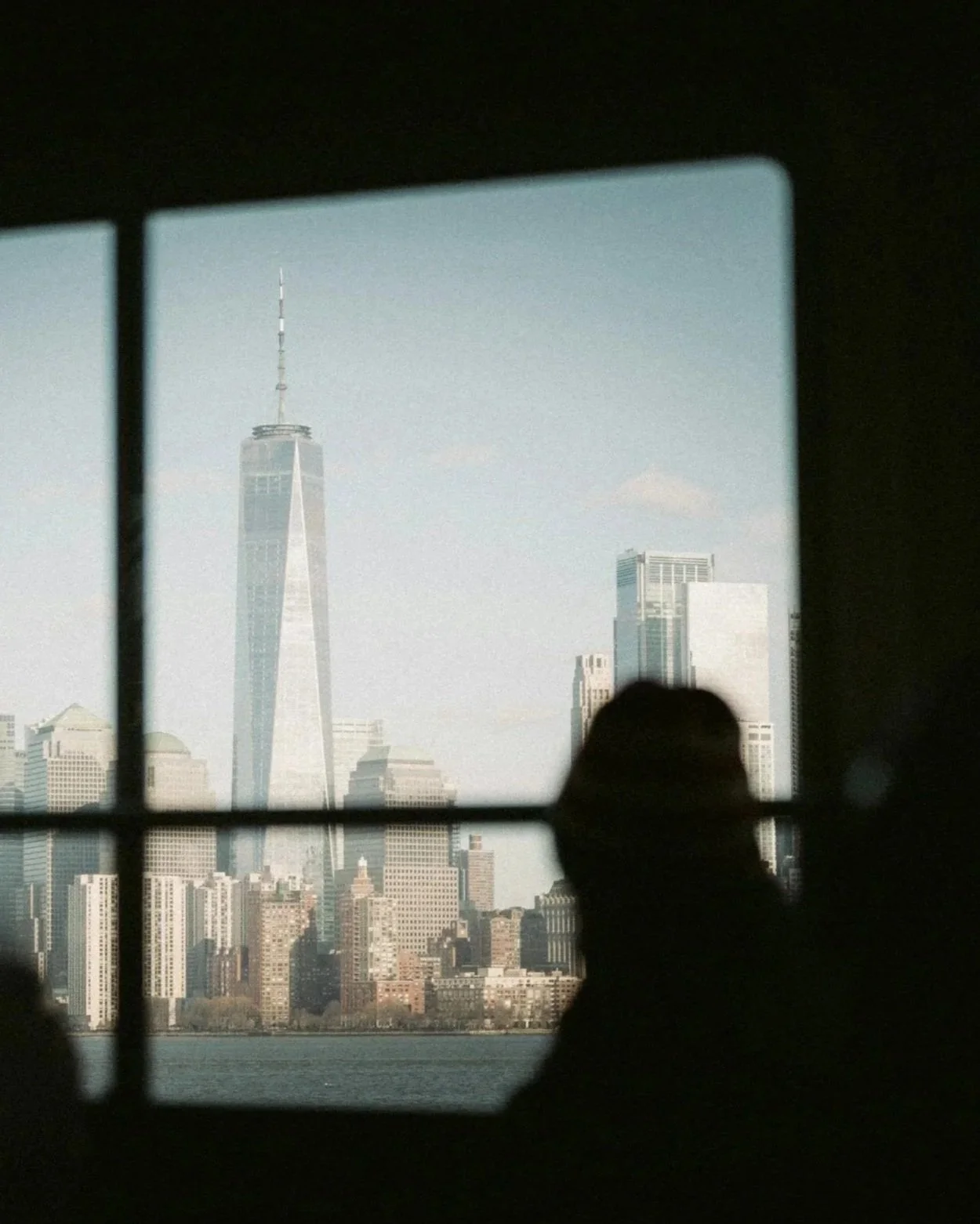 View of the New York City skyline through a window, with soft silhouettes in the foreground, representing perspective and reflection in urban life.