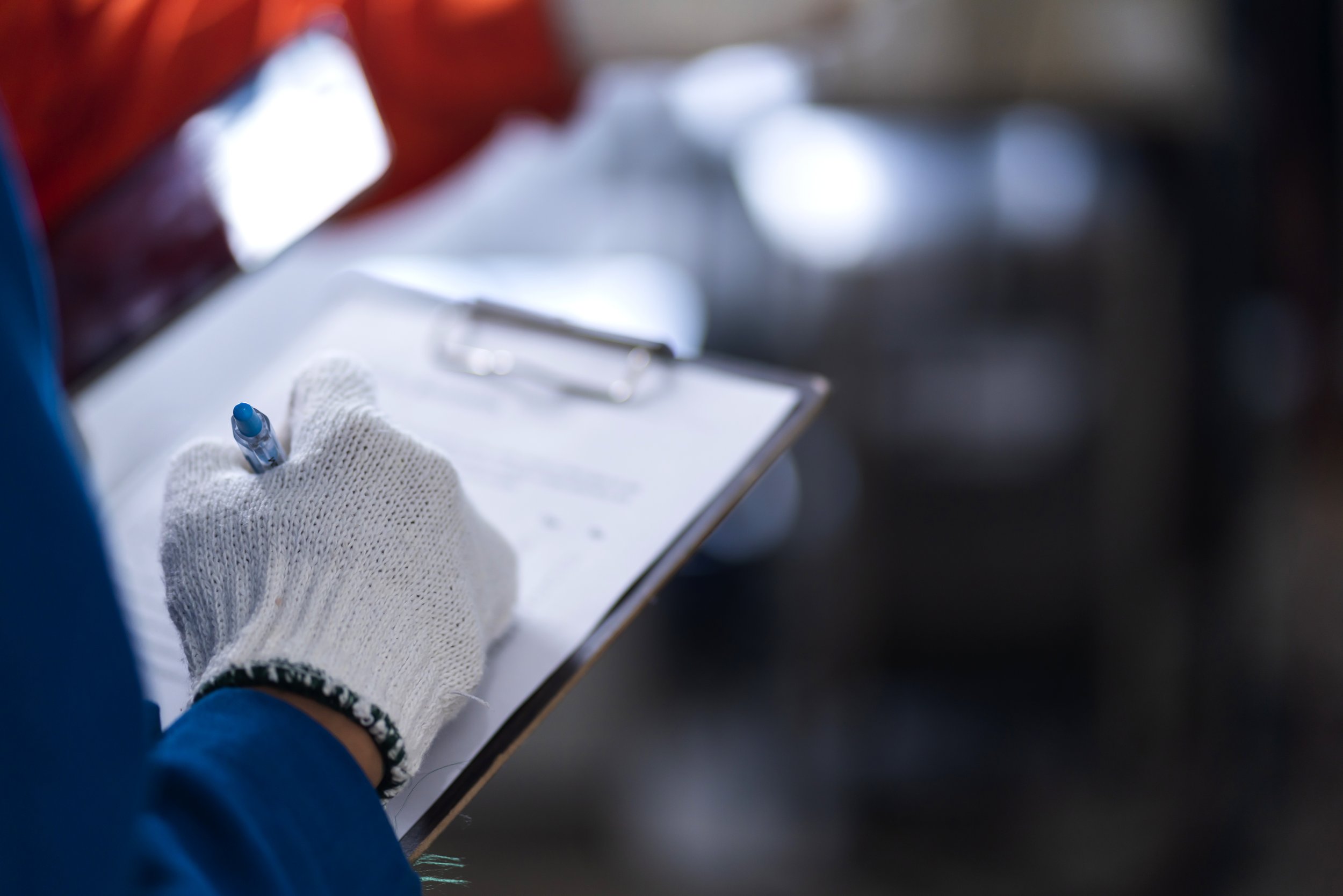 Person in a white glove writing or signing on a clipboard with a blue pen.