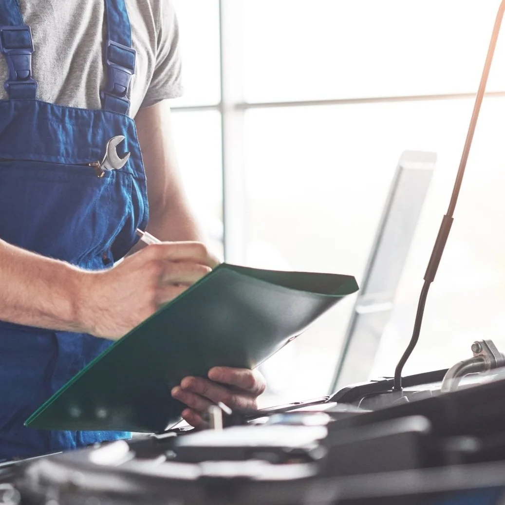 A person wearing a work uniform and a tool pocket on their chest writing in a clipboard, with equipment and a microphone in the foreground.