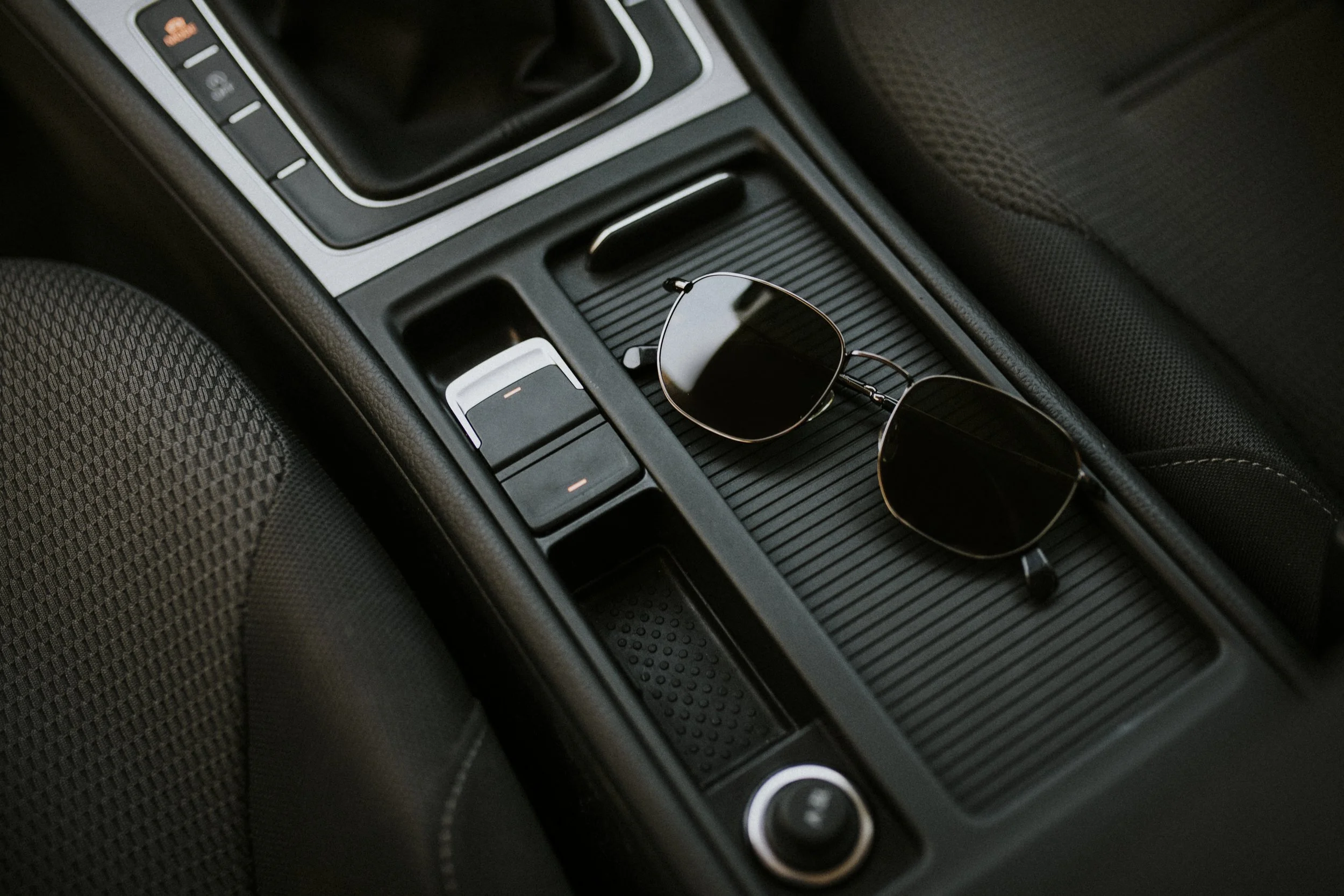 Sunglasses placed on the center console of a car with gear shifter and other controls.
