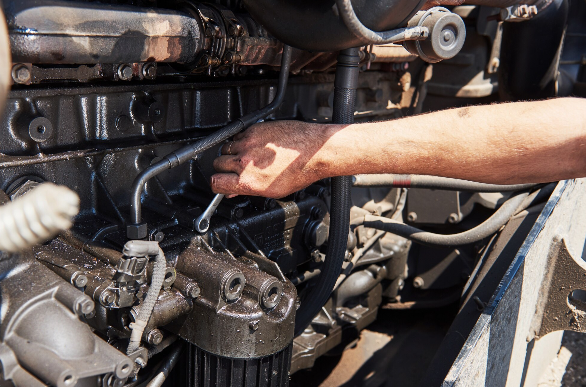 A person repairing or working on an engine, using their right hand to adjust a component in the engine bay of a vehicle.