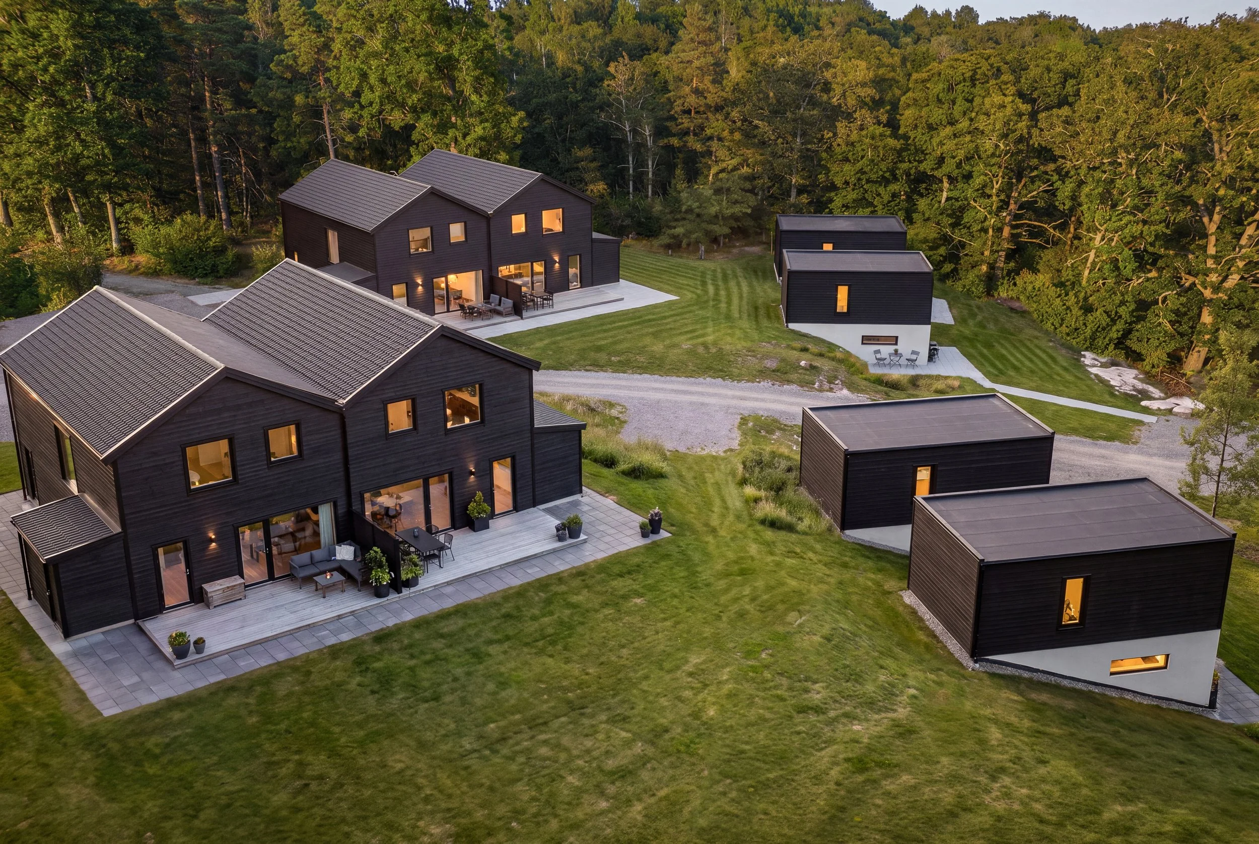 En modern villa i skogsomgivning, sett från luften, med uteplatser och gräsmattor mellan byggnaderna.