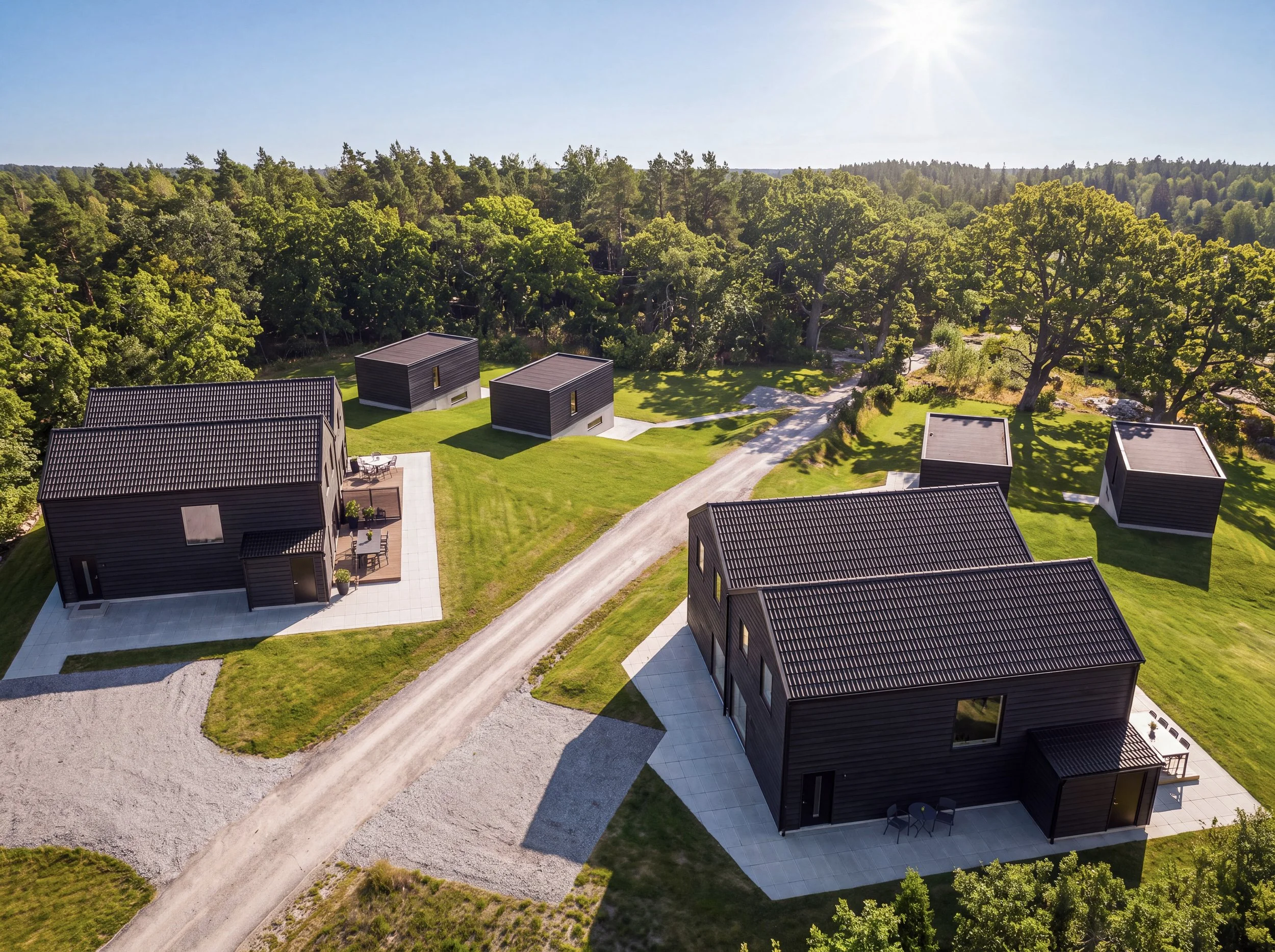 Fjärde generationens moderna små fritidshus i svart trä, omgivna av en grönyta och omgivande skog i bakgrunden, under en klar solig dag.