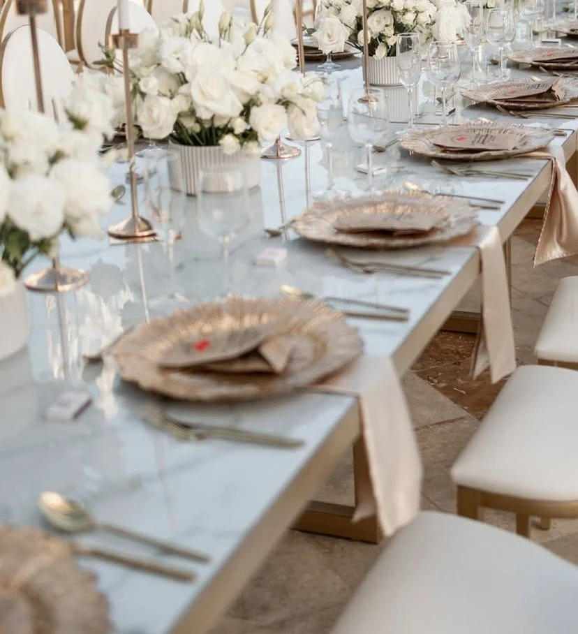 Mesa decorada para evento con vajilla elegante, copas, flores blancas y centros de mesa.