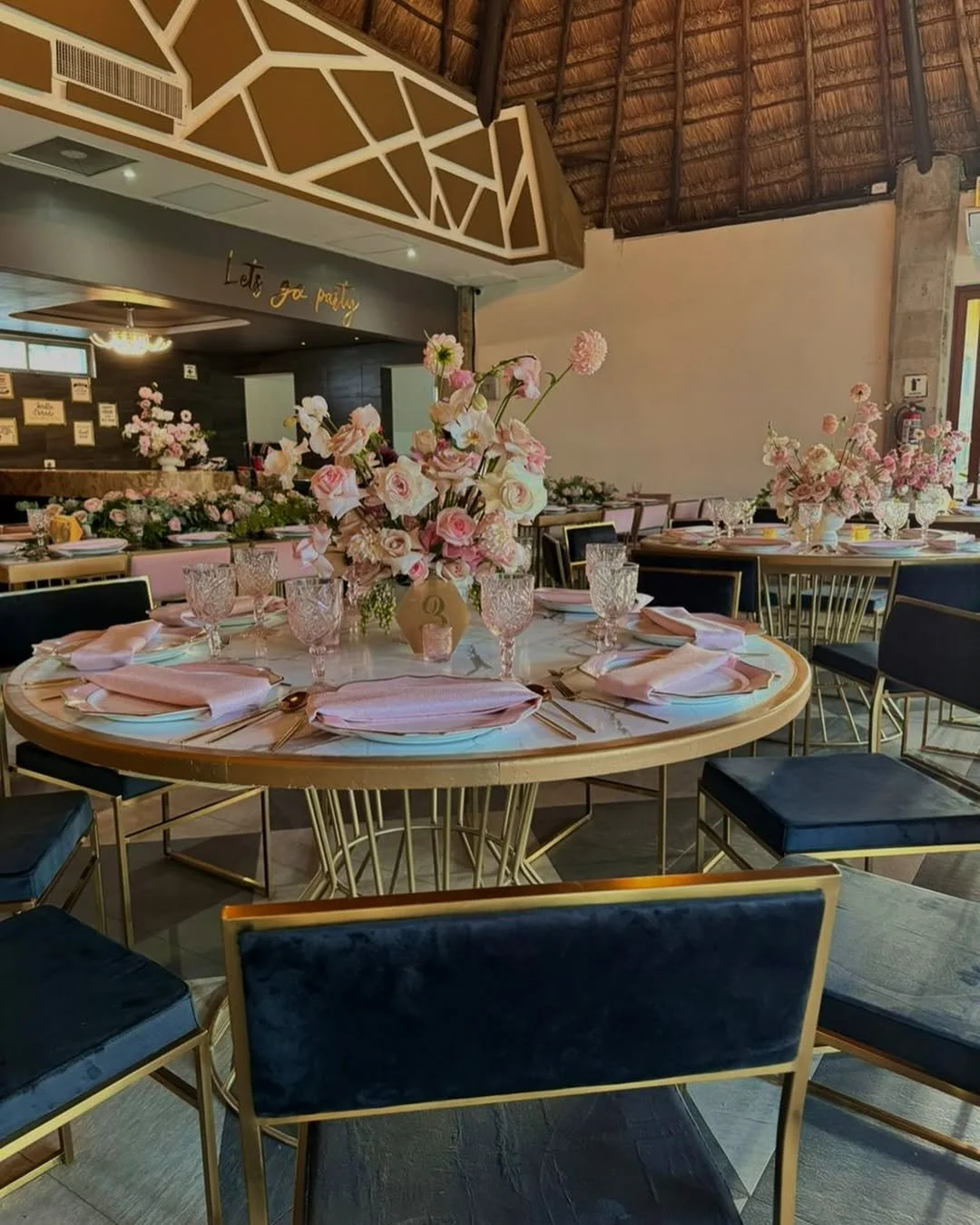 Mesa decorada con flores rosadas en jarrones, platos, copas de cristal, cubiertos y manteles rosados en un salón con temática elegante y decoraciones florales para evento especial.