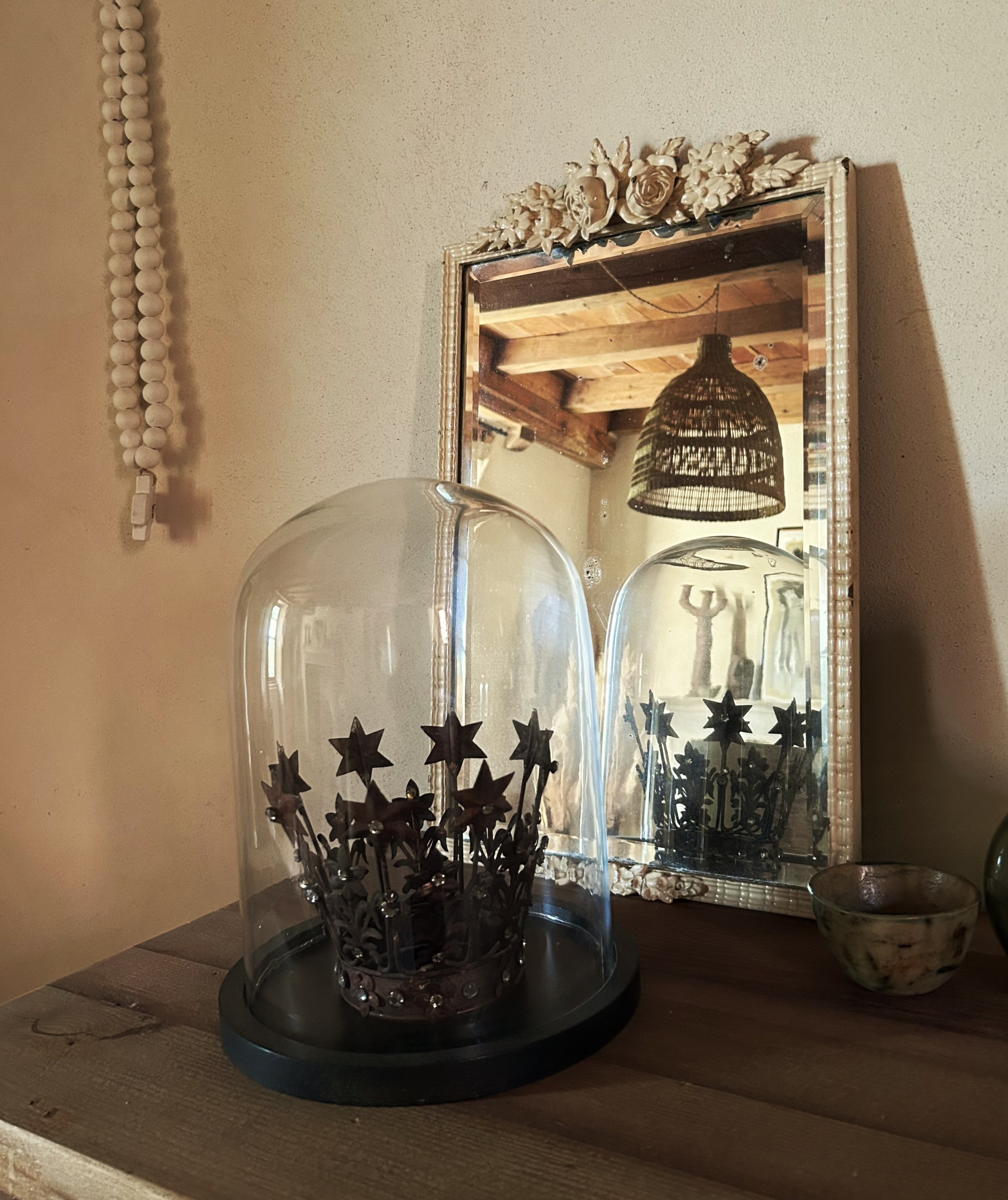 Deux boules en verre transparent avec des décorations en formes d’étoiles et de sapins en métal noir positionnées sur une table en bois. Derrière, un miroir orné de fleurs en relief et un luminaire en osier suspendu.