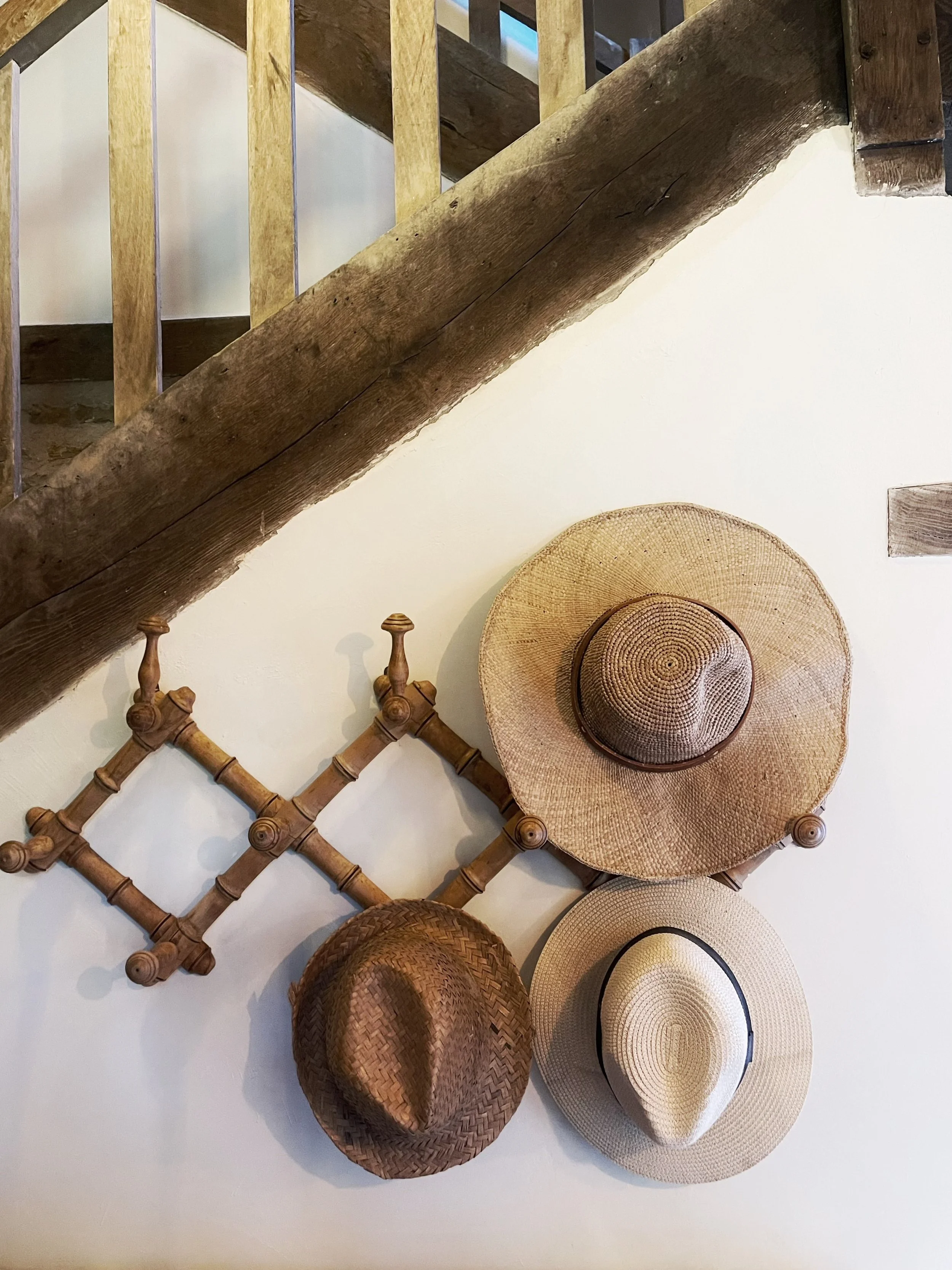 Un mur blanc avec plusieurs chapeaux en paille de différentes formes et couleurs suspendus dessus.