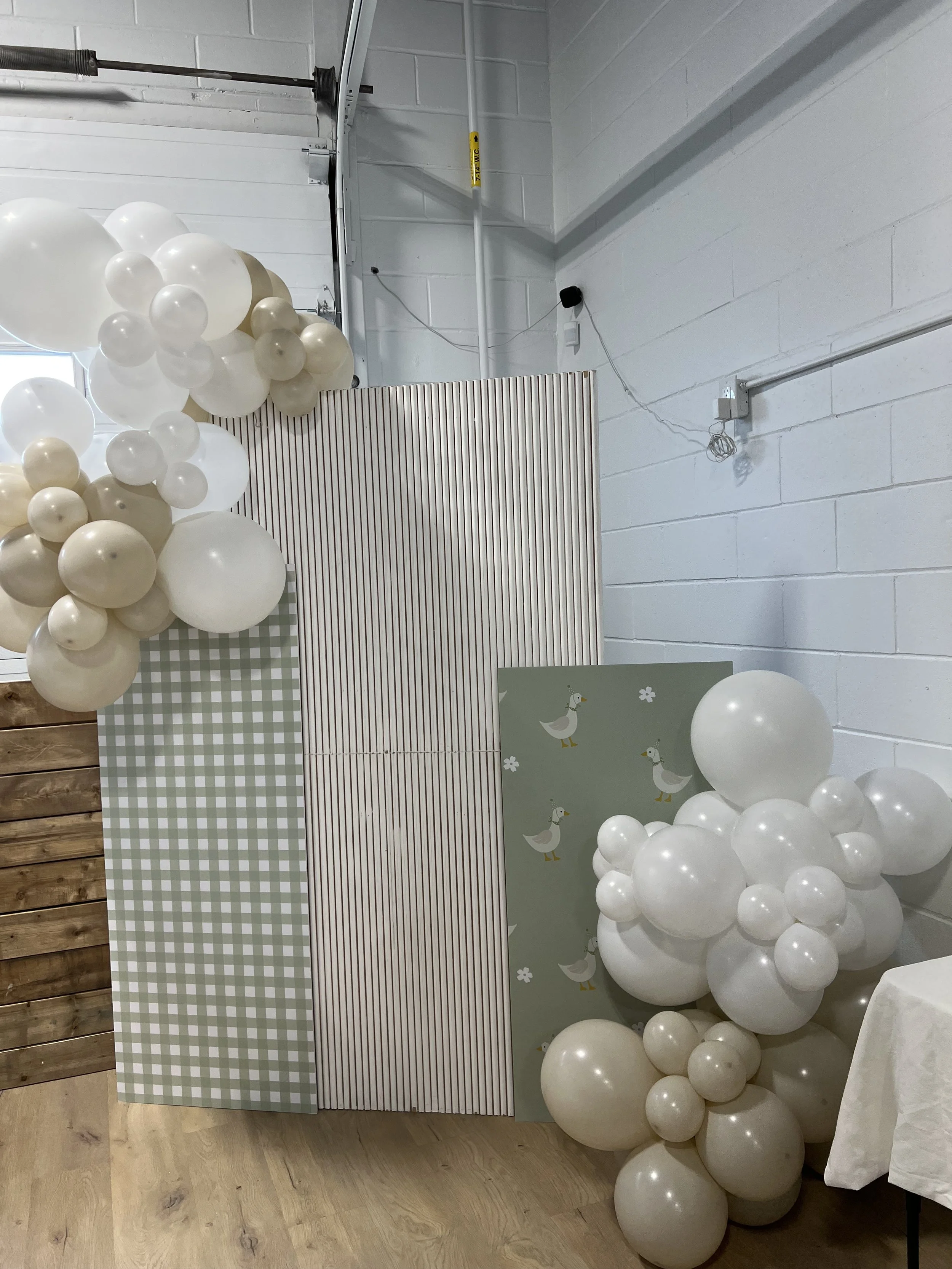 Decorative setup with white balloons, patterned panels, and a duck-themed backdrop, likely for a celebration or event.