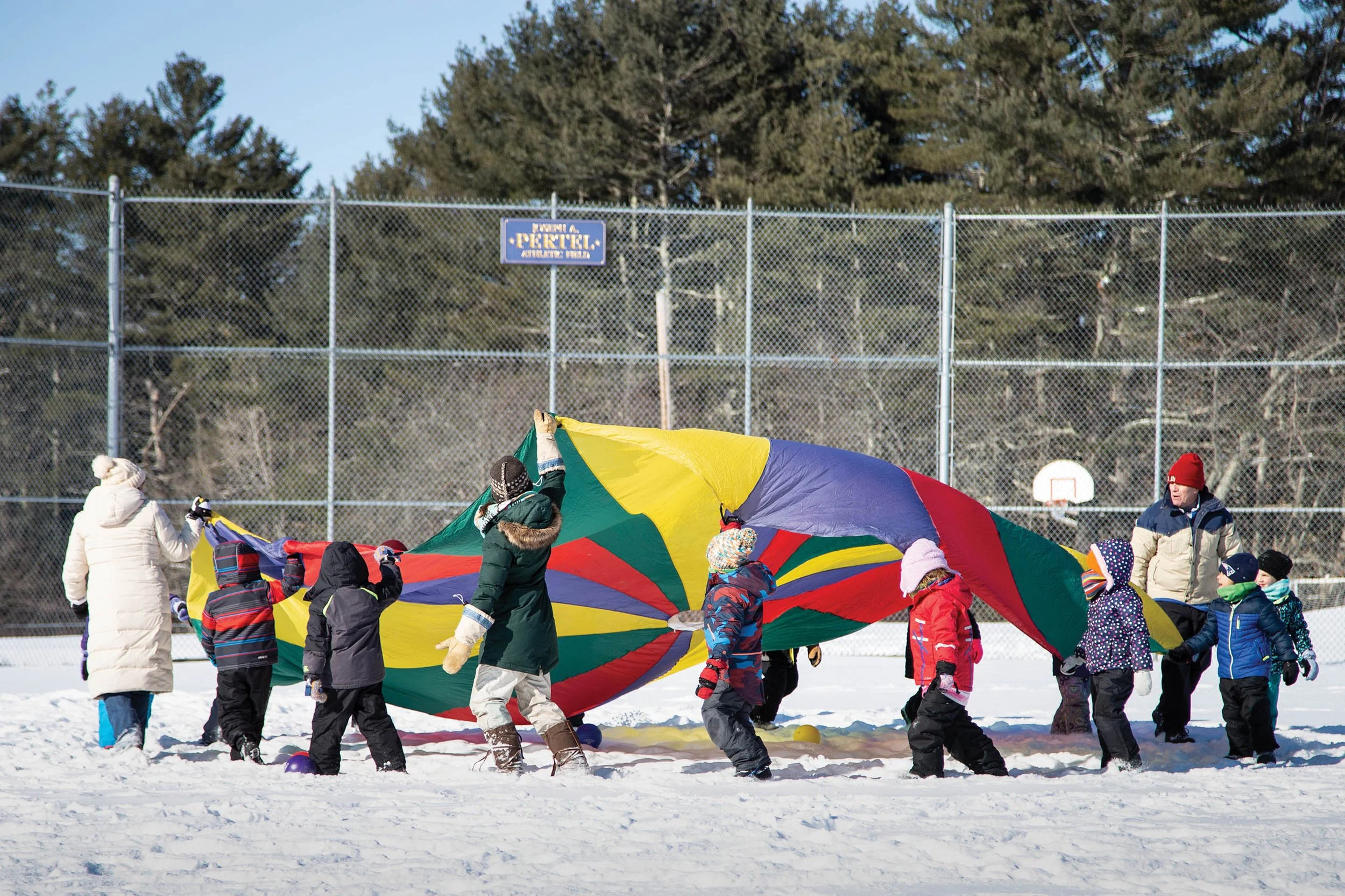 Kids circled around parachute playing on a snowy playground.