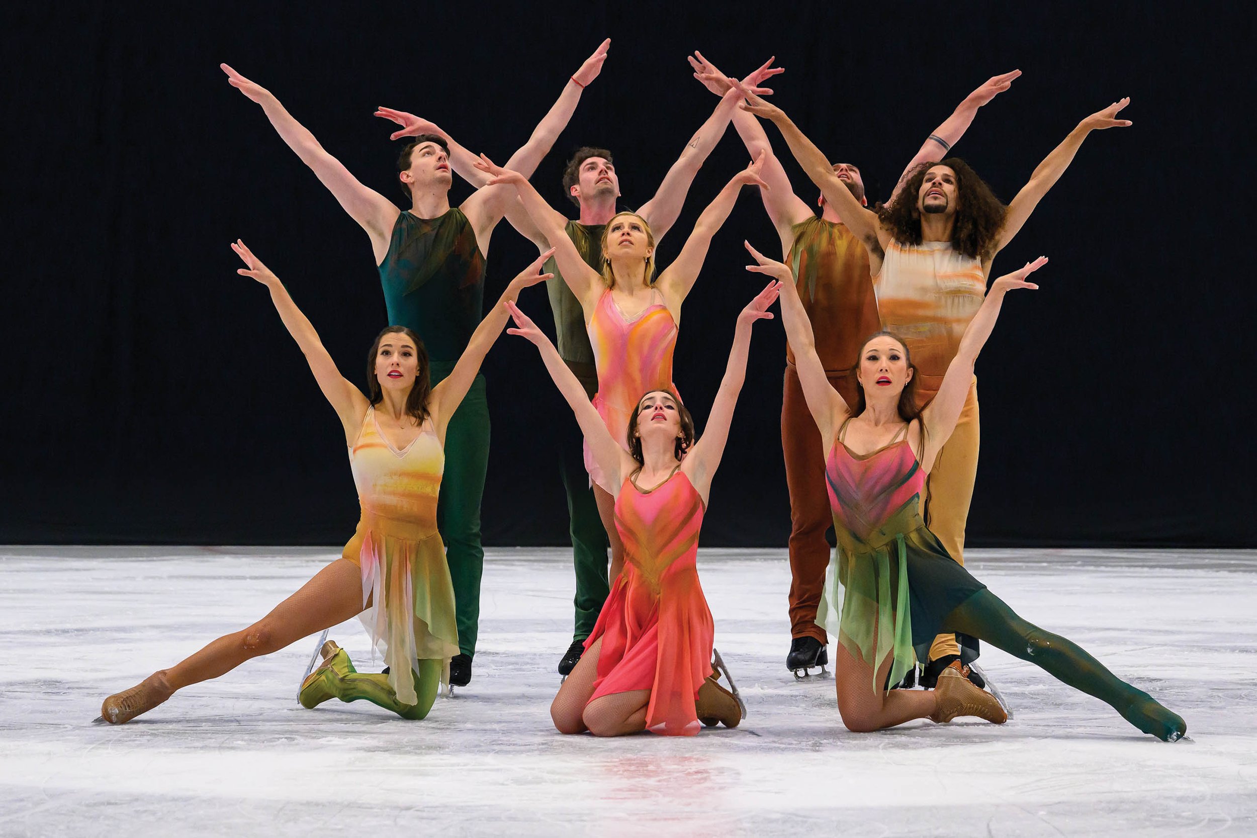 Ice skaters with arms overhead gathered against a black background.