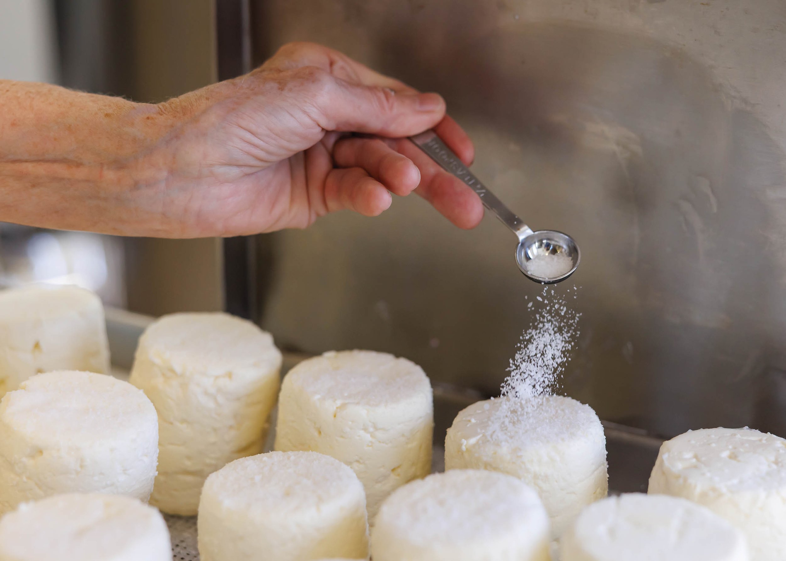 Hand sprinkling salt over mounds of cheese.