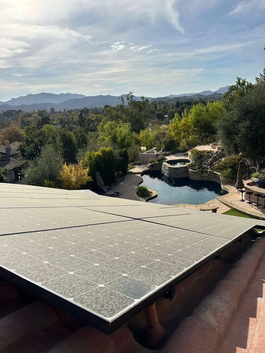 View from roof showing solar panels, pool with hot tub, lounge chairs, trees, and mountains in the background.