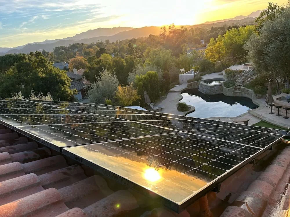 Solar panels installed on a roof with a view of a backyard pool area during sunset.