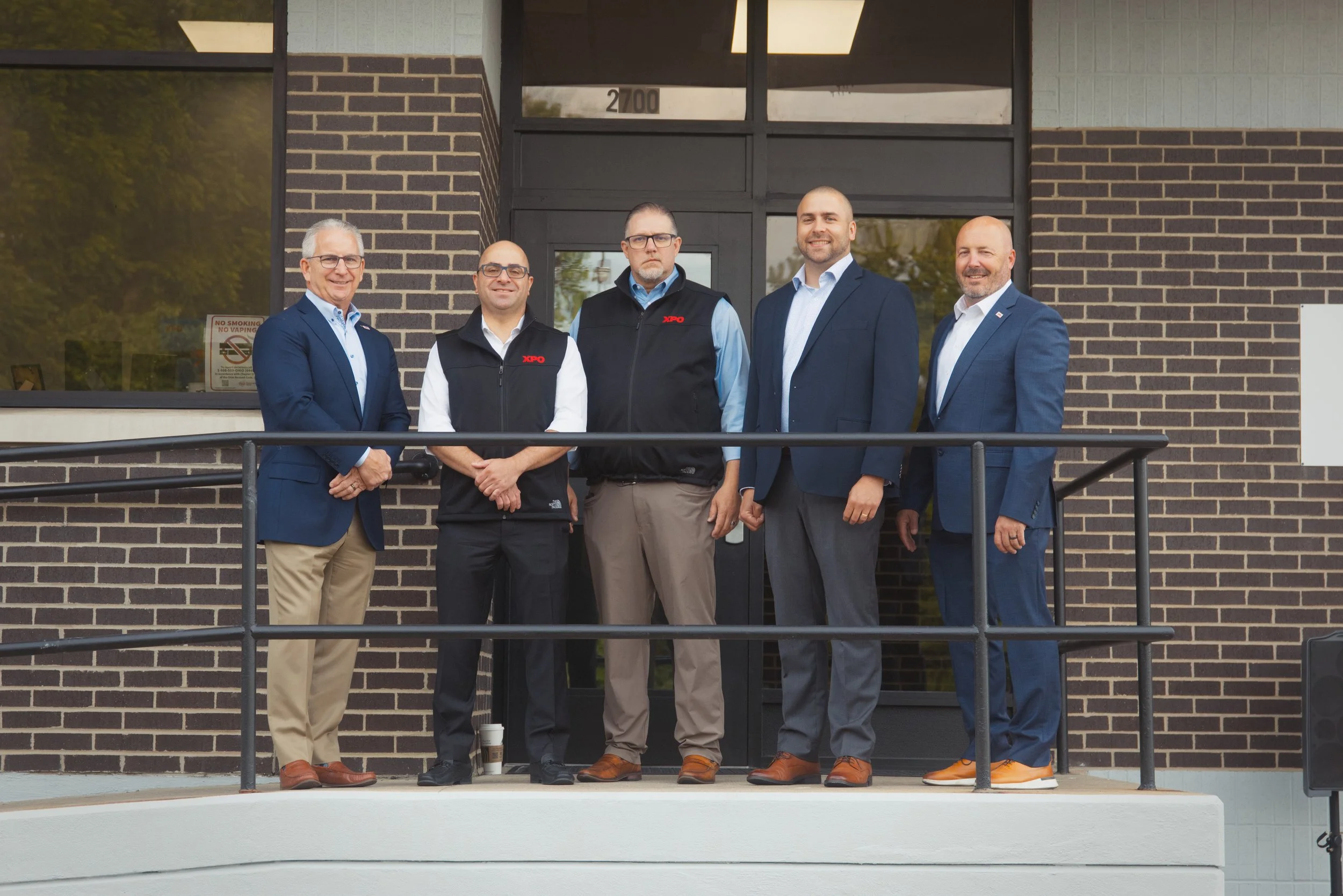 Top executives and managers of a large freight company pose at the grand opening of a new location, captured with natural lighting and professional cameras.