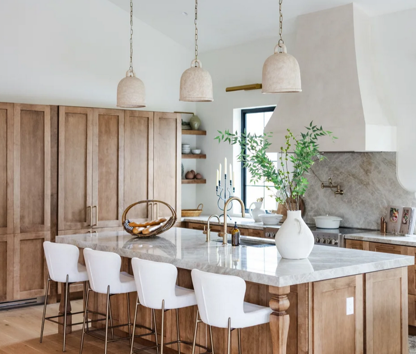 A white vase with textured details filled with dried yellow flowers on a wooden stand on a granite tak mahal countertop in a modern kitchen.