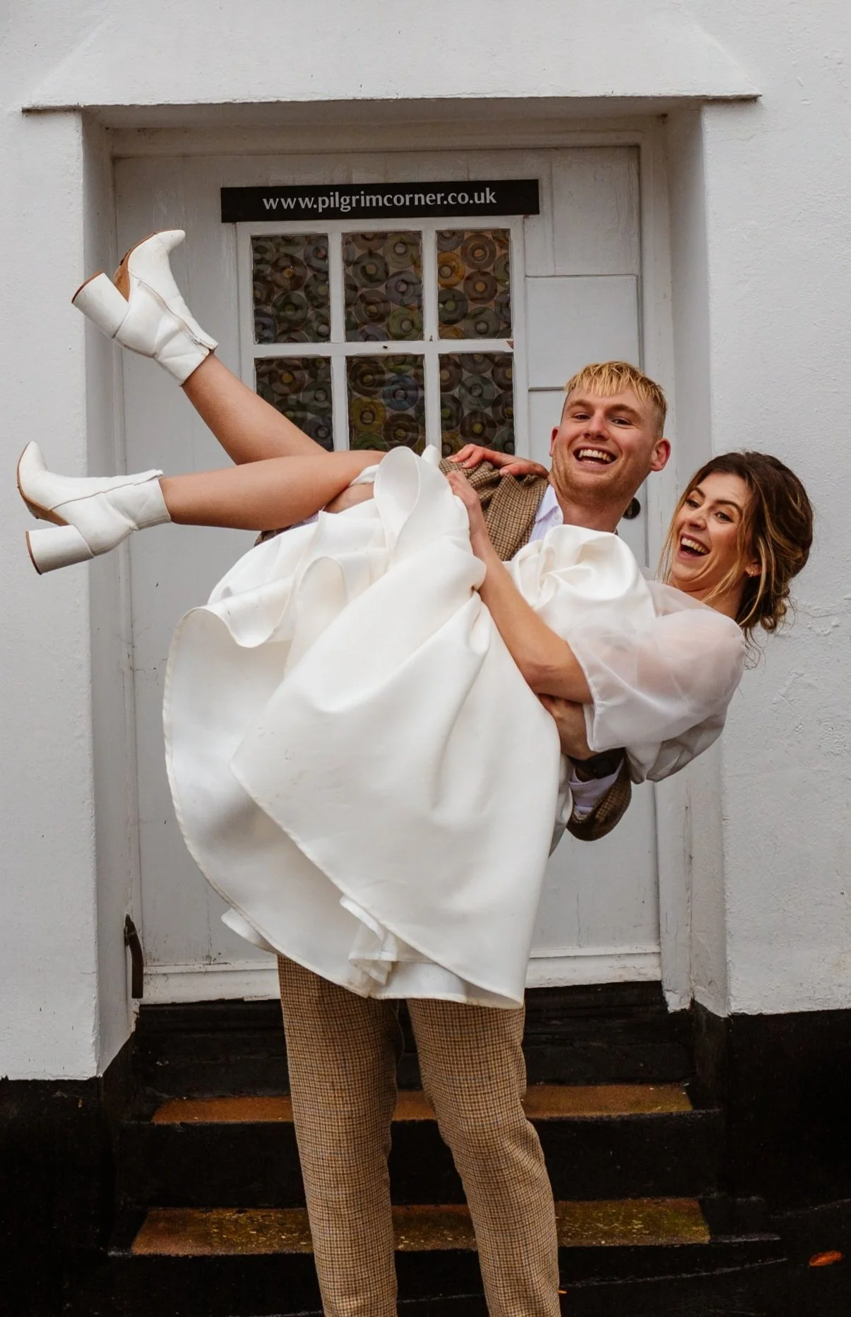 A bride in her wedding dress being held by her new husband in the doorway to Pilgrim Corner, a beautiful small wedding venue on the edge of Exmoor