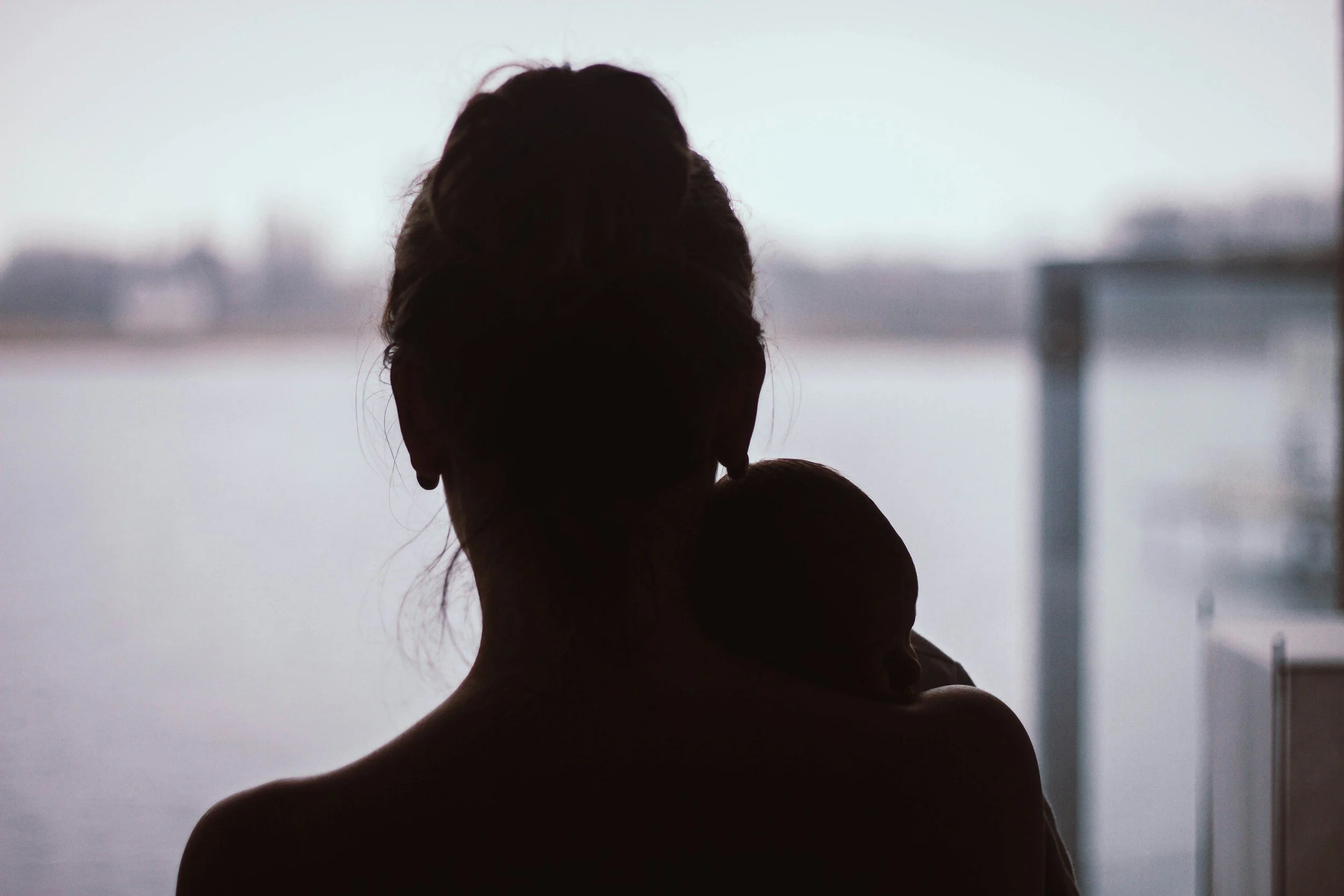 Silhouetted woman with her baby. She has postpartum depression, postpartum anxiety, postpartum rage. She has relationship strains during parenthood. Disconnected with her partner.