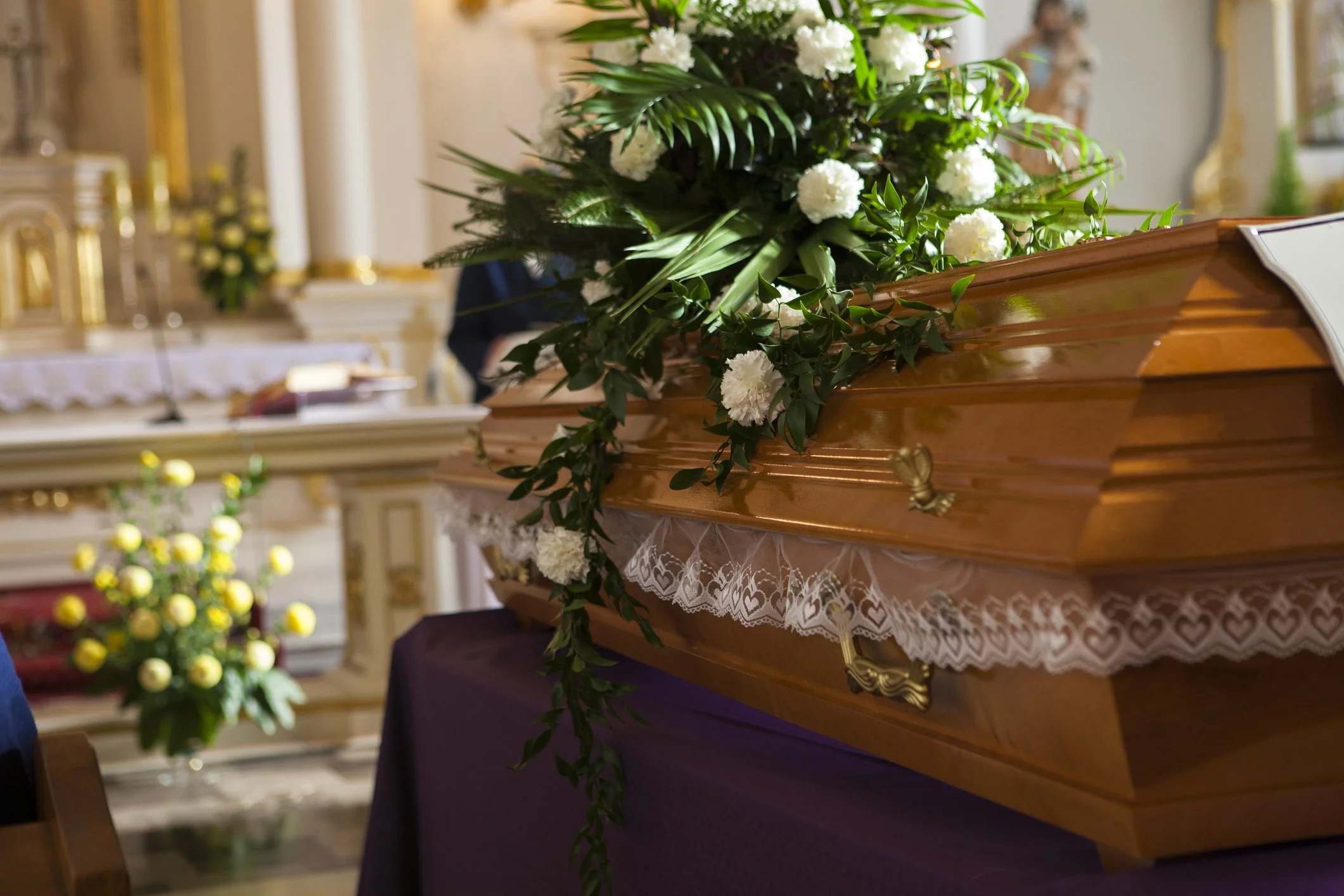 Wooden casket adorned with white flowers and greenery in a church setting.