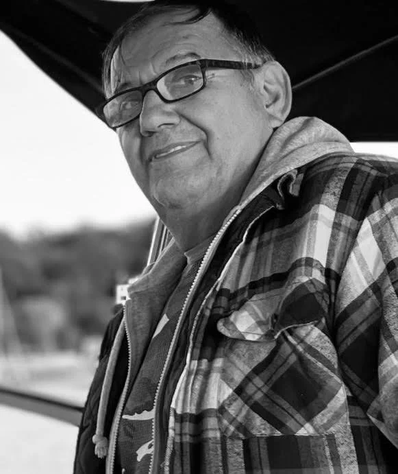 Black and white photo of a person wearing glasses and a plaid jacket, looking to the side.