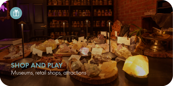 Display of various mineral and crystal specimens with labels, illuminated by warm lighting, in a retail or museum setting.