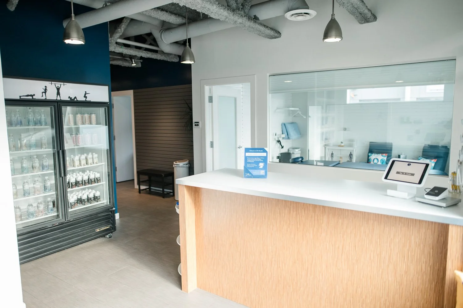 Interior view of a modern dental office reception area with a wooden counter, glass door, and beverage refrigerator stocked with drinks.