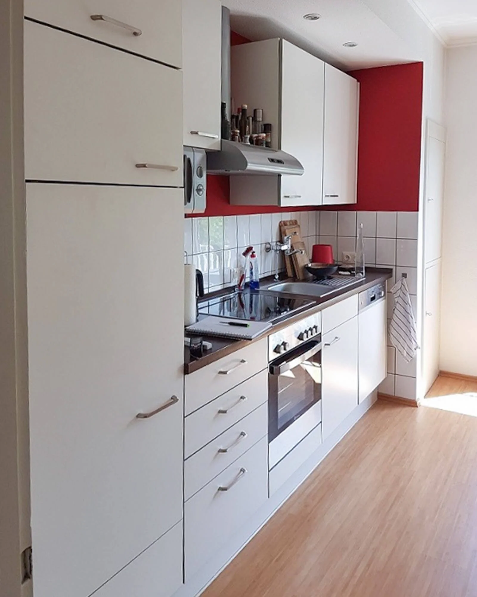 Vorher-Situation einer Küche mit roten Wänden, weißen Fronten und klassischem Fliesenspiegel in einer Kölner Wohnung.