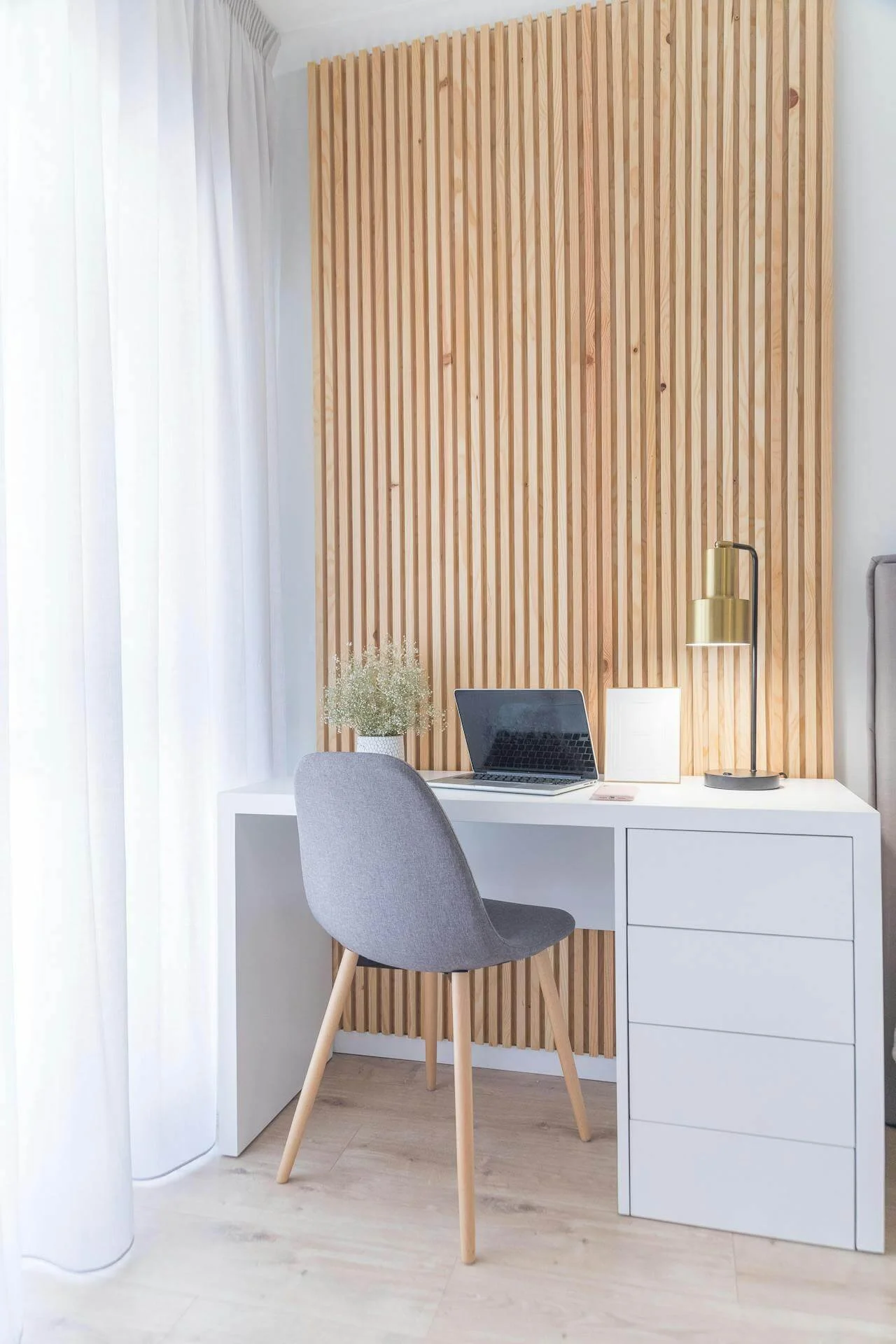 Kompaktes Homeoffice mit Holzlamellenwand, weißem Schreibtisch und wohnlicher Akustiklösung.