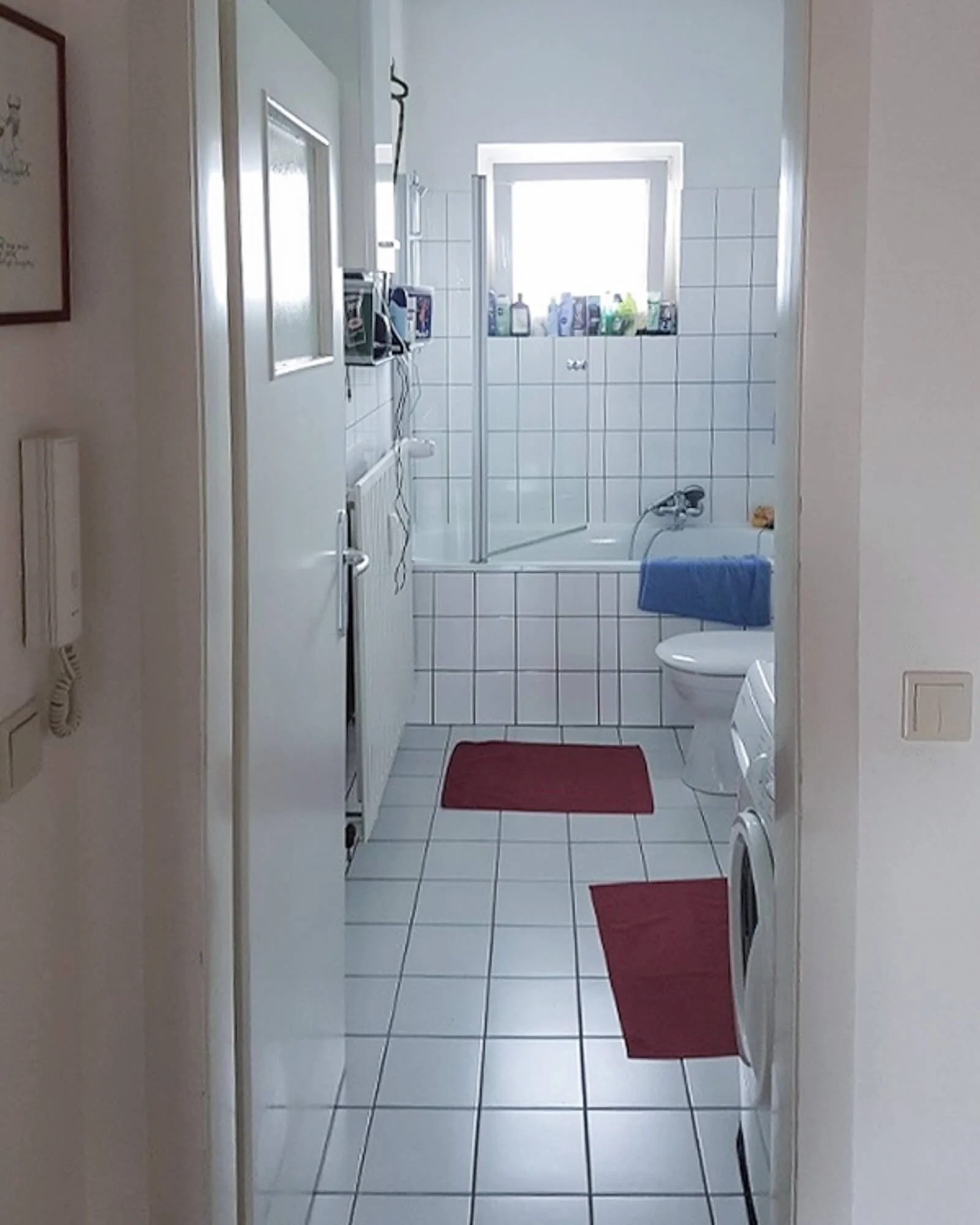 Vorher-Situation eines Badezimmers mit weißen Rasterfliesen, Badewanne und Waschmaschine in einer Kölner Eigentumswohnung.