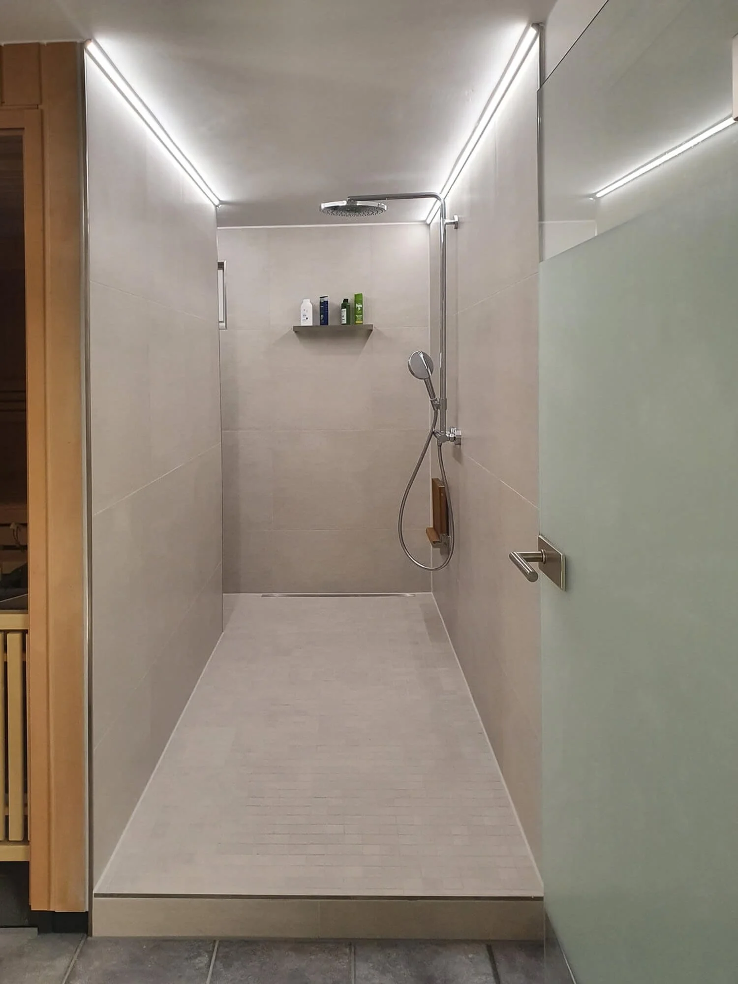 Moderne, bodengleiche Walk-In-Dusche mit großformatigen beigen Fliesen und integrierten LED-Lichtleisten.