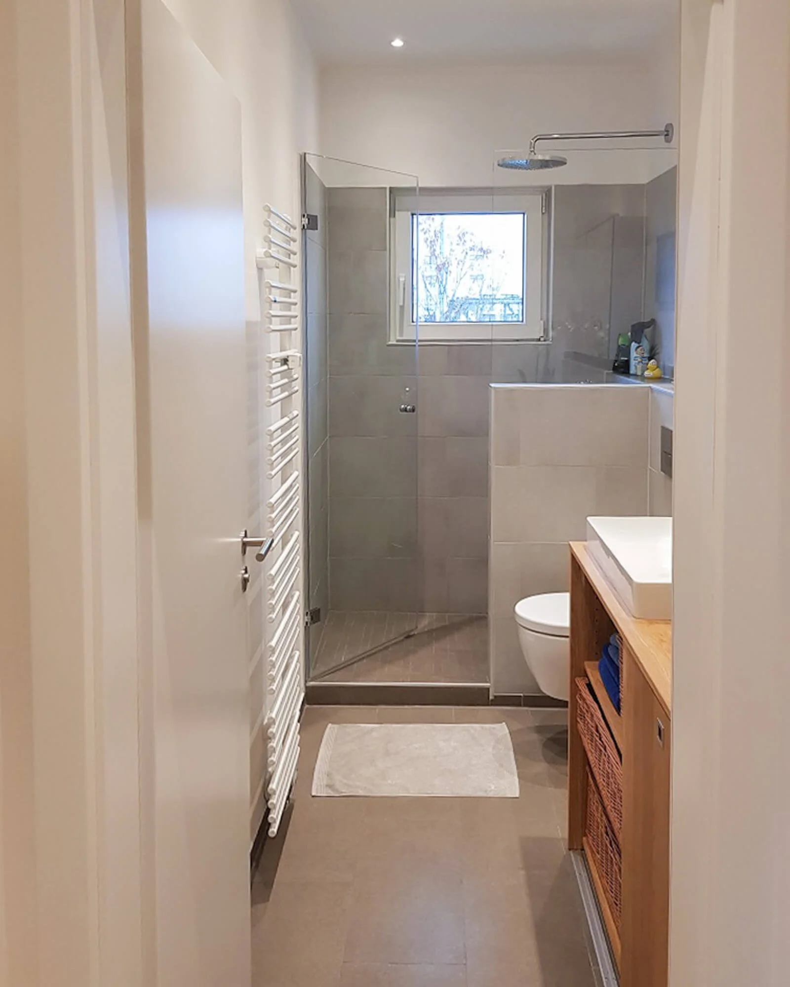 Modernisiertes Badezimmer mit bodengleicher Dusche, Glaswand und großformatigen grauen Fliesen in einer Kölner Eigentumswohnung.