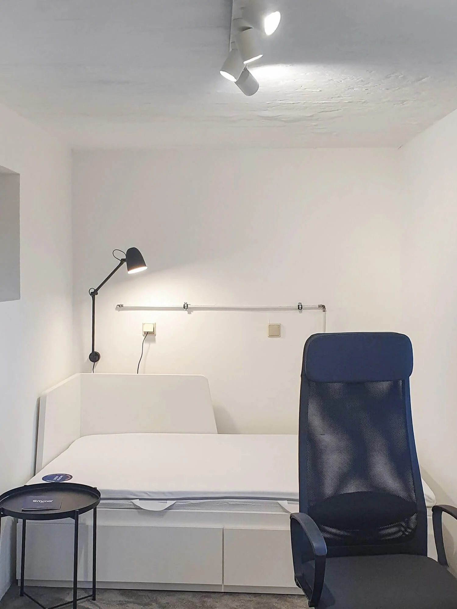 Ausgebautes Gästezimmer im Keller in Köln mit einem weißen Stauraumbett, grauem Teppich und moderner, gezielter Beleuchtung, geplant von Berthe Dong.