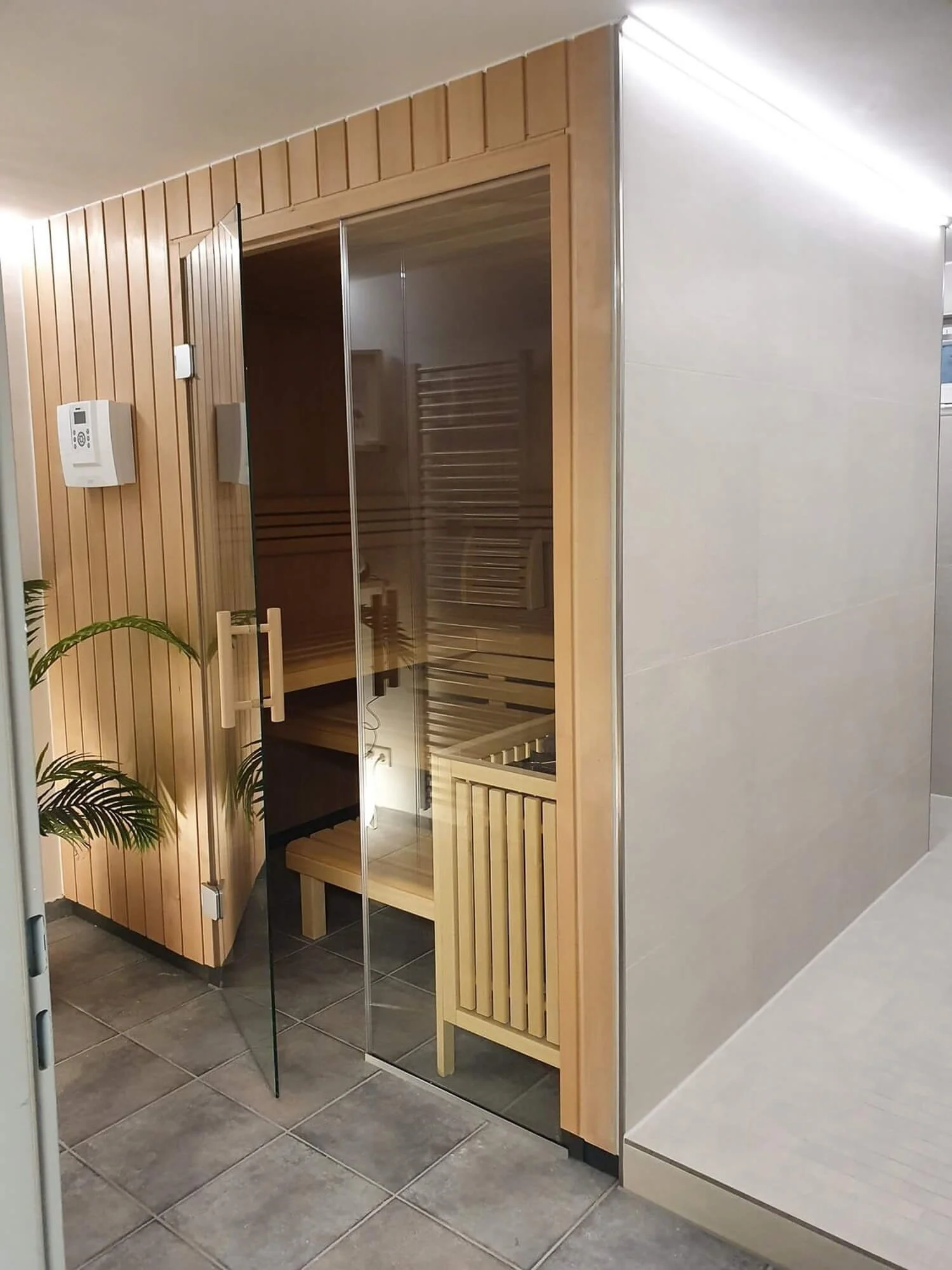Moderne Holzsauna mit rahmenloser Glasfront neben einem hochwertig gefliesten Duschbereich in einem privaten Keller-Spa in Düsseldorf, geplant von Berthe Dong.