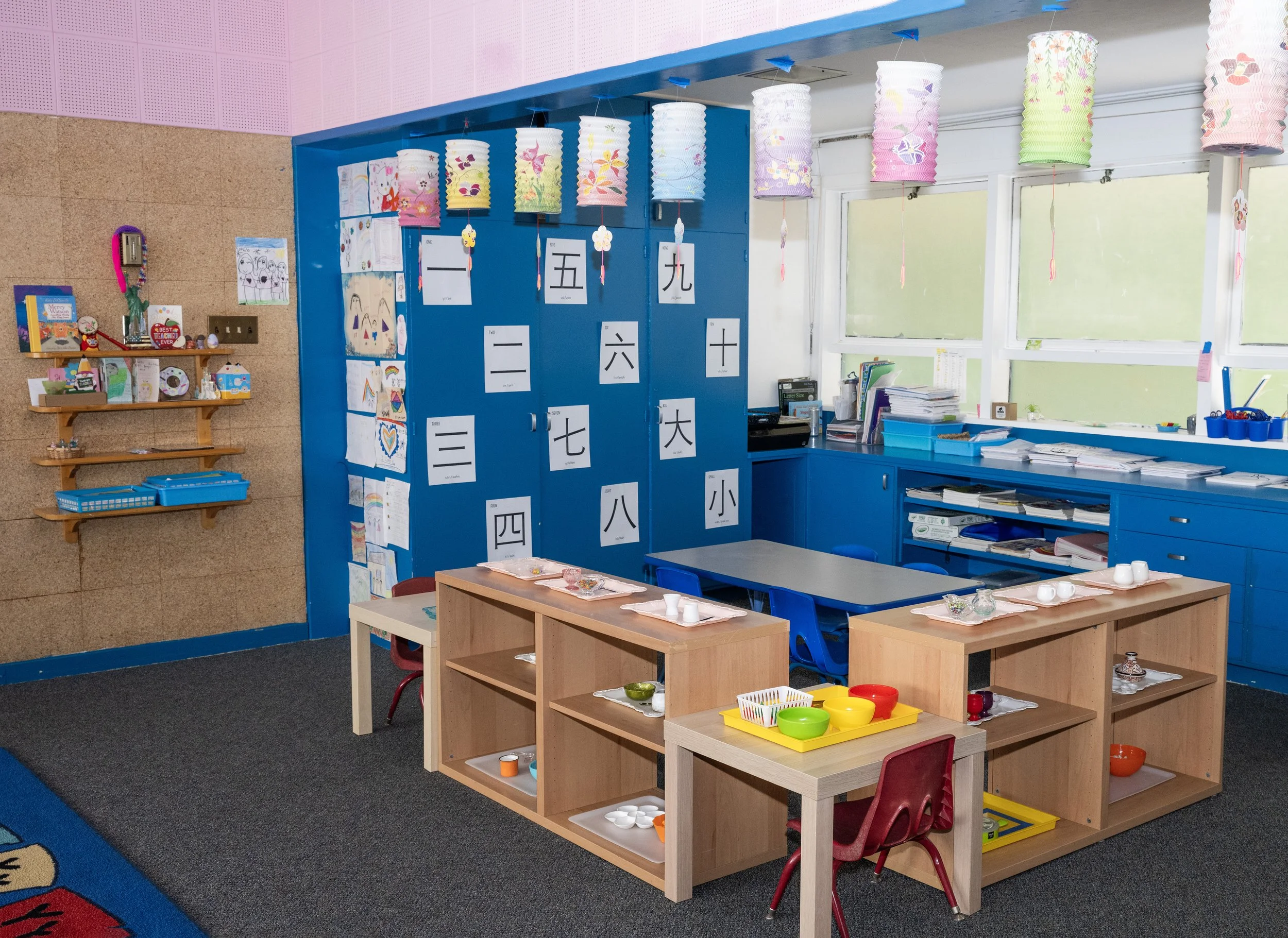 Colorful classroom with Japanese characters on the wall, small tables with cups and bowls, and paper lanterns hanging from the ceiling.