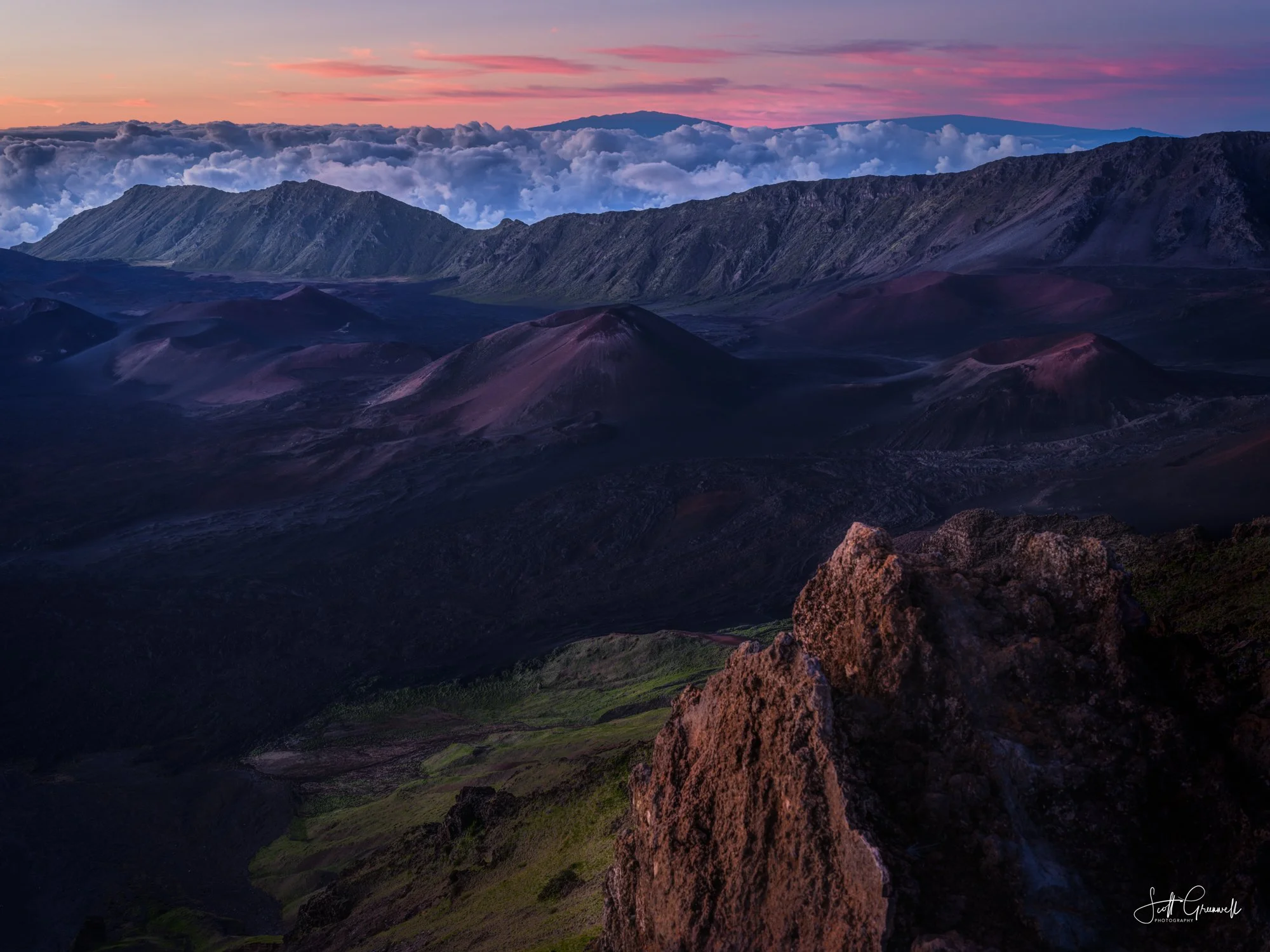 Sunrise over the volcanic crater of Haleakalā National Park in Maui, Hawaii, with cinder cones beneath pink skies and a dramatic sea of clouds.