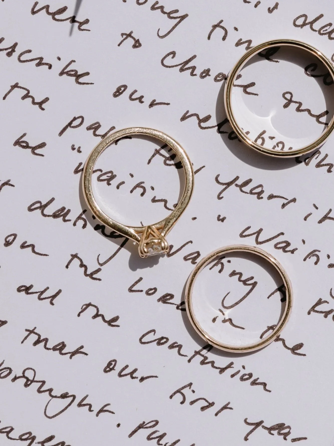 Three gold rings, one set with a diamond, placed on a handwritten letter at villa wedding venue in Tuscany Italy.