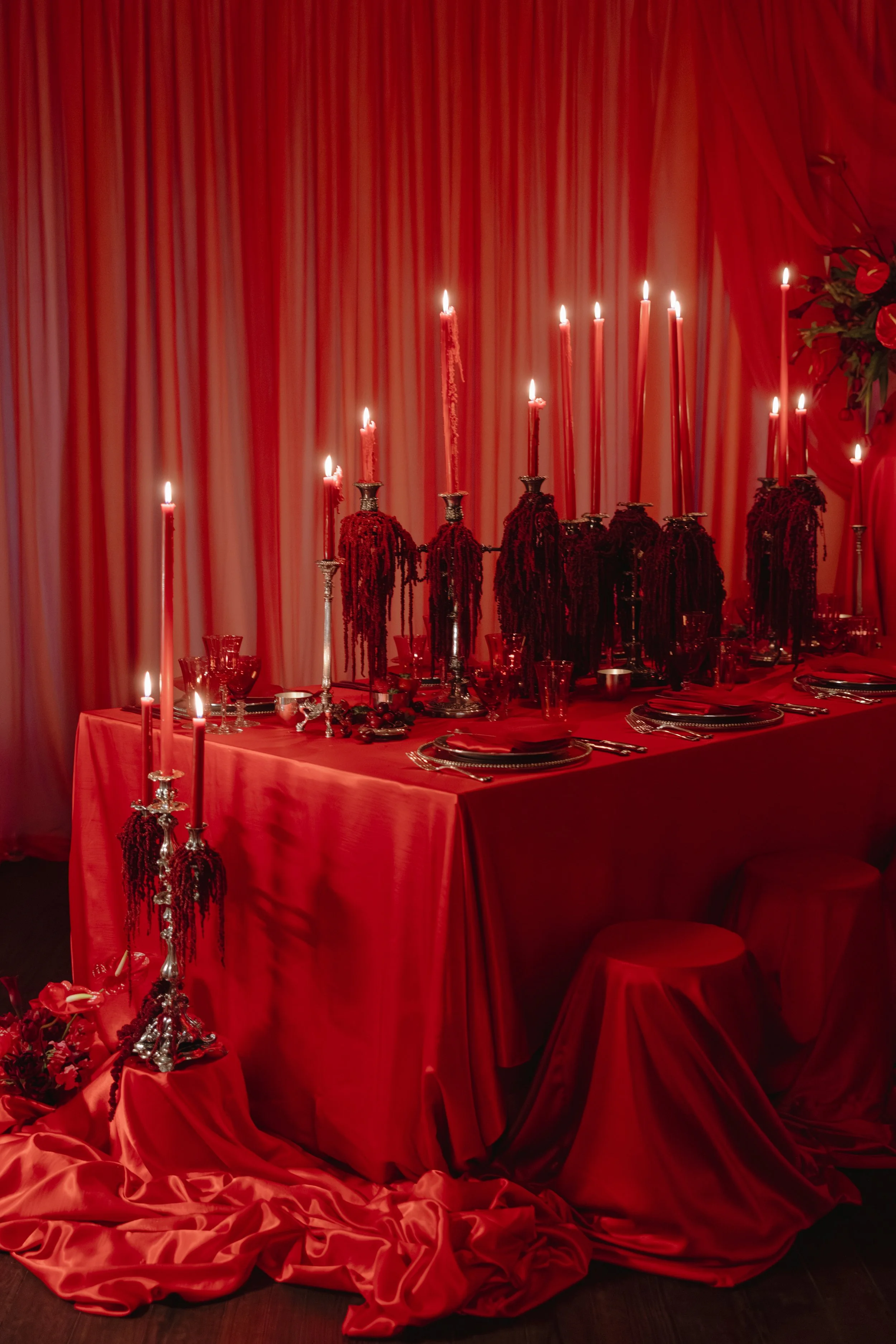 A table set for a formal gathering with red drapery, tall red candles, and elaborate silver candleholders for a wedding reception in Charleston, South Carolina.