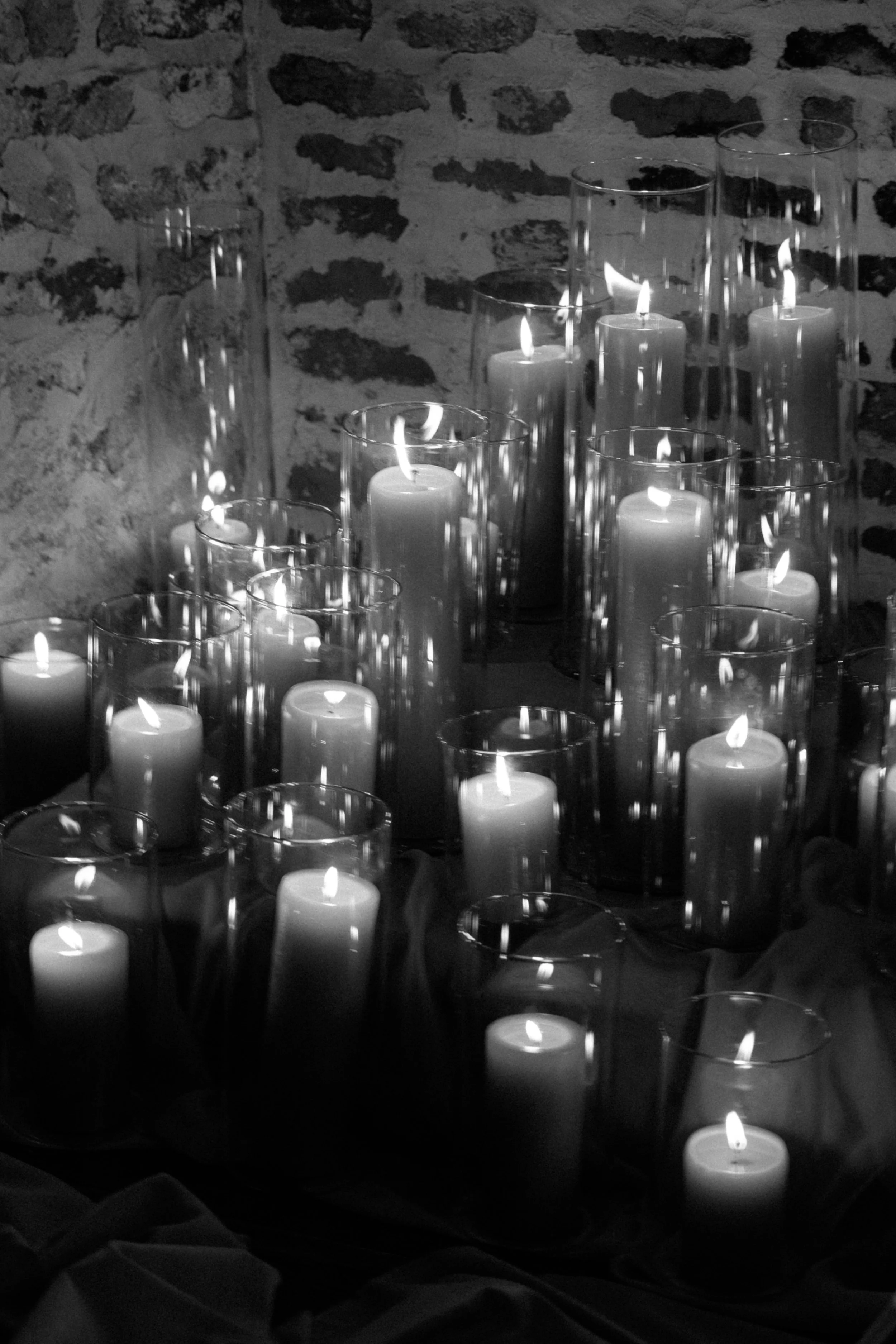 Several lit candles inside glass holders arranged on a surface in front of a textured brick wall,  for a wedding reception in Charleston, South Carolina.