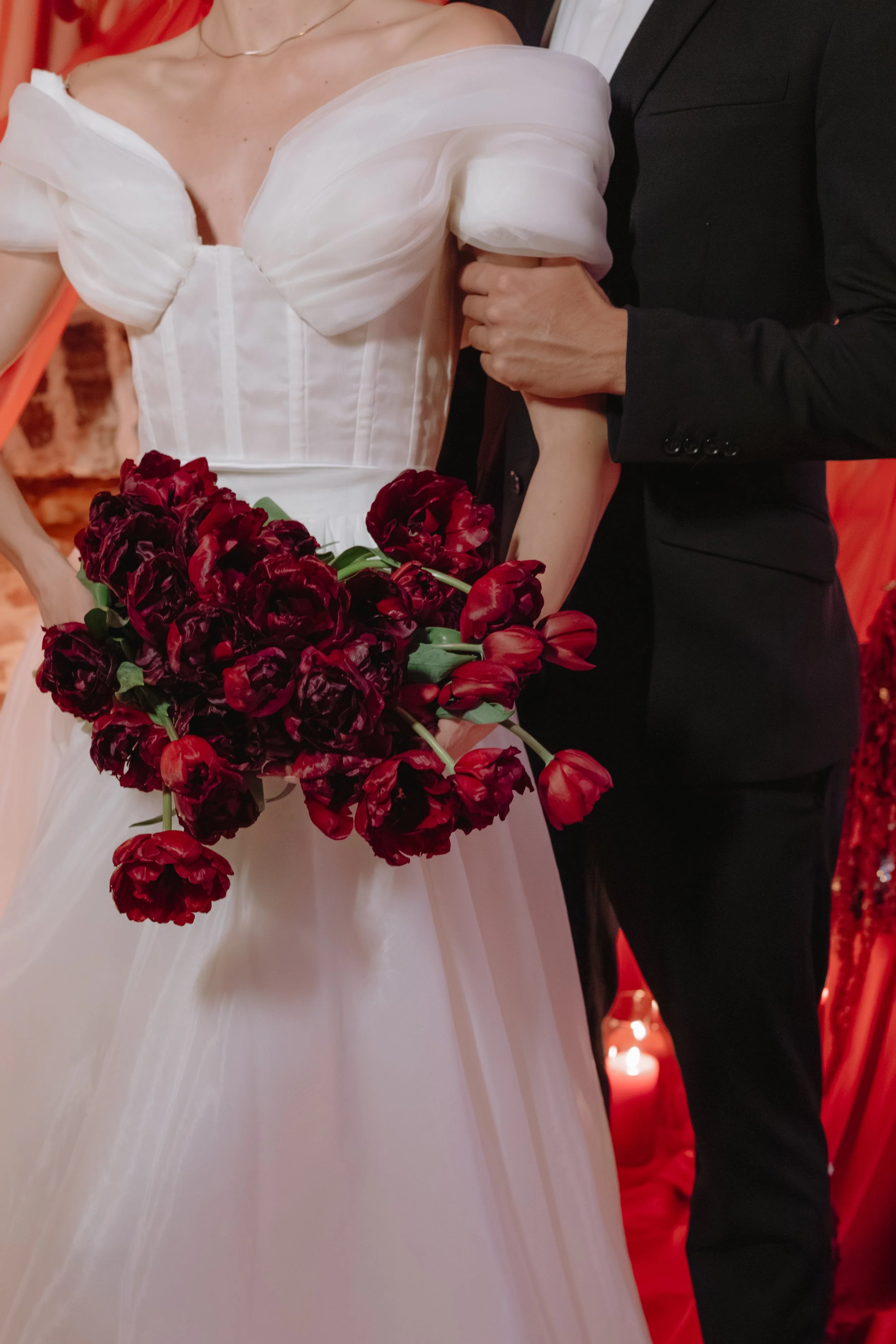 A bride in a white wedding dress holding a bouquet of red and purple flowers, standing next to a groom in a black suit, at a wedding ceremony or reception for a wedding reception in Charleston, South Carolina.