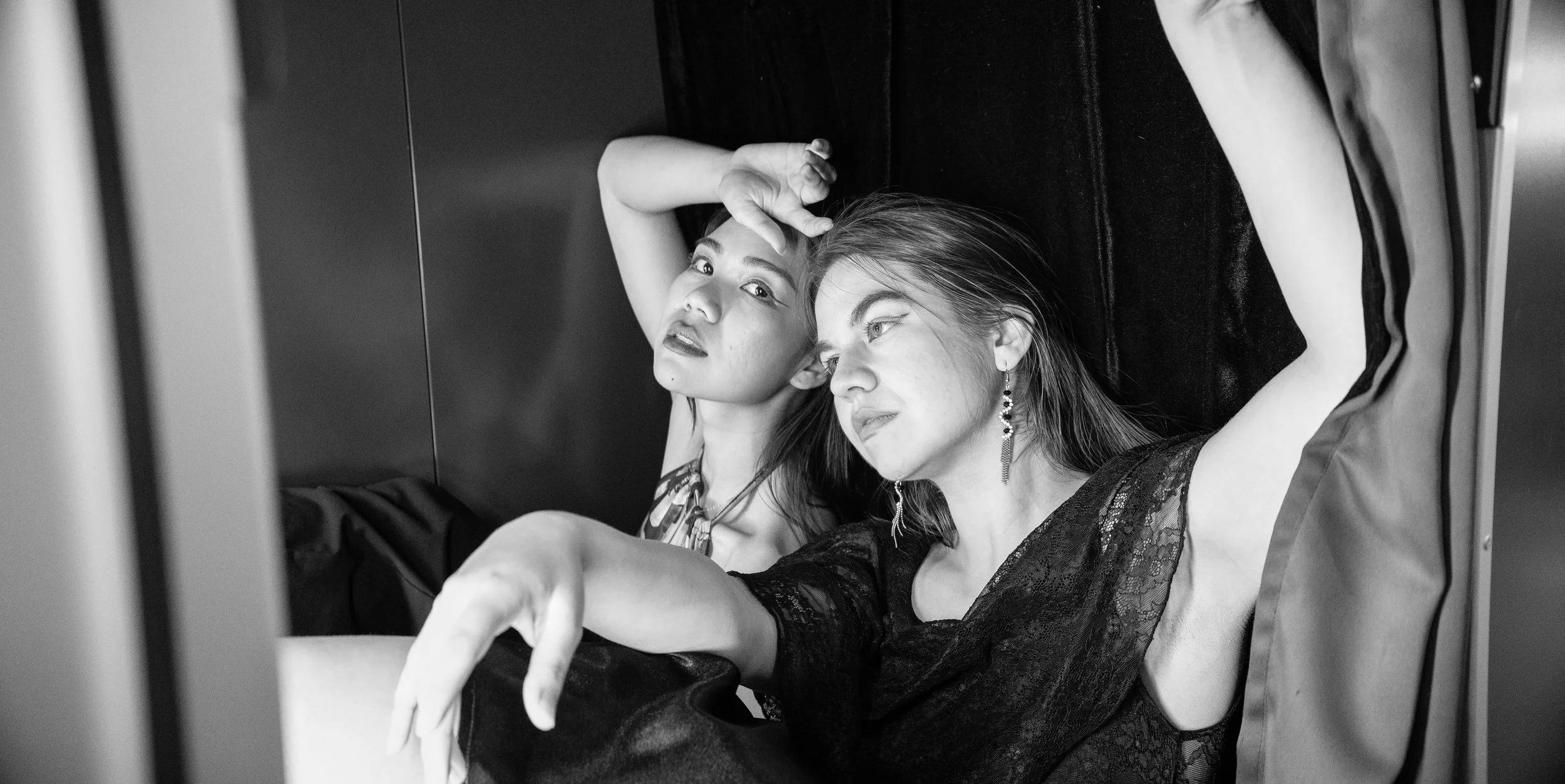 Two women lying down, facing the camera, in black and white. One woman has her hand on her forehead and the other is looking intently, both with relaxed expressions.