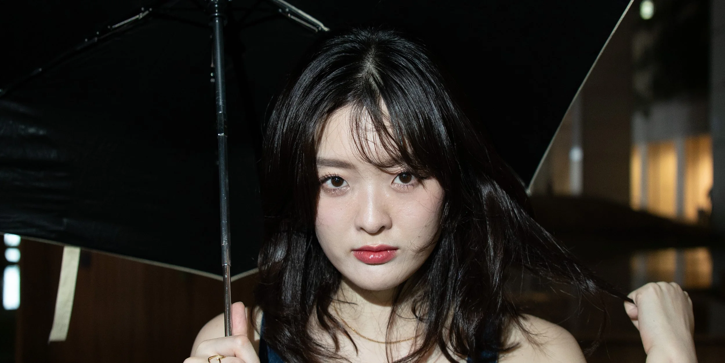 A young woman with dark hair holding a black umbrella outdoors at night.