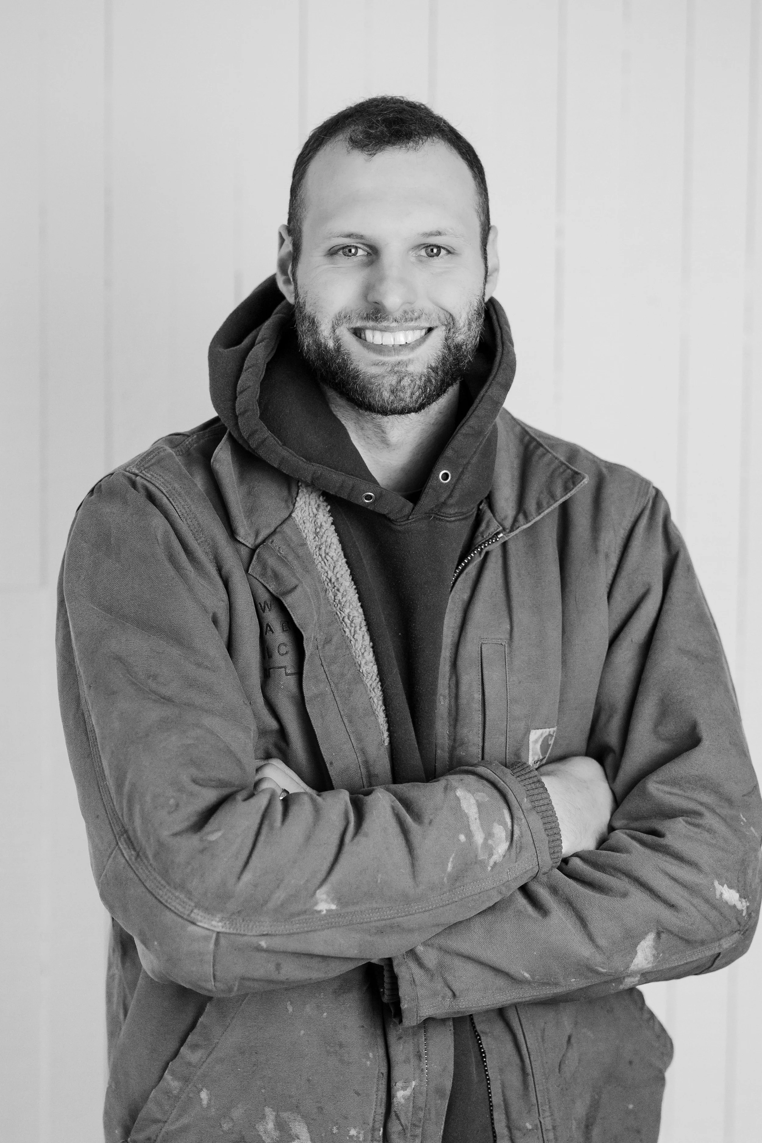 Man wearing a Clarkbuilt sweatshirt, smiling, standing against a textured wall.