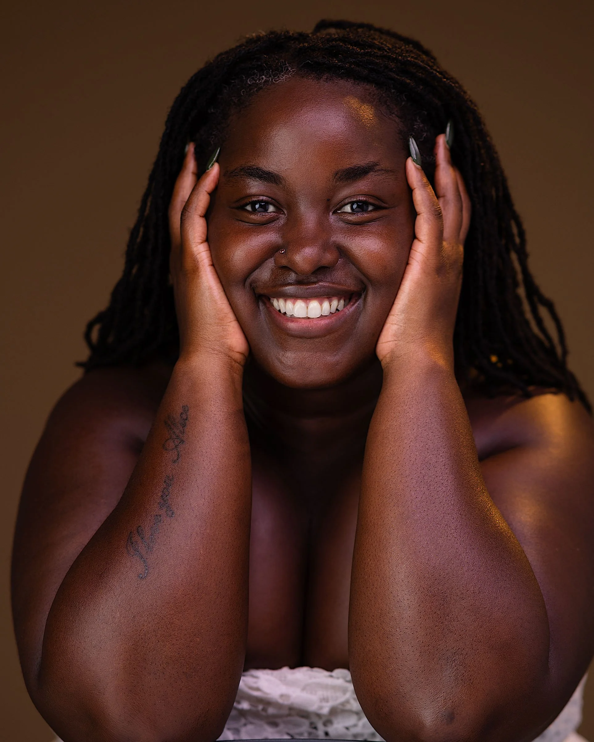 Alice smiling at the camera with her hands resting against her temples, against a warm brown background.