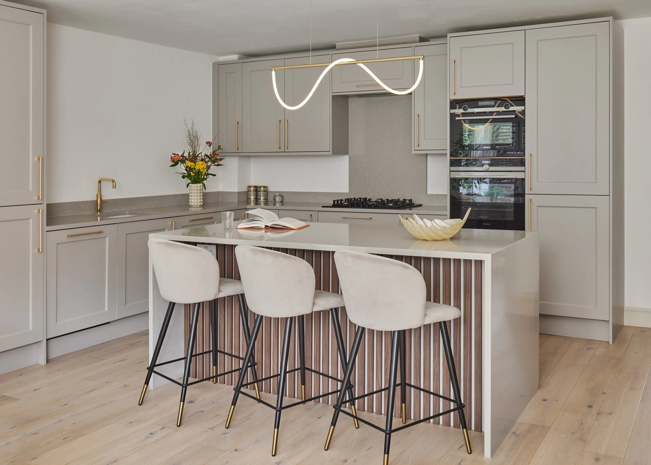 Wimbledon modern kitchen interior with beige cabinets, marble countertops, and sleek bar stools.
