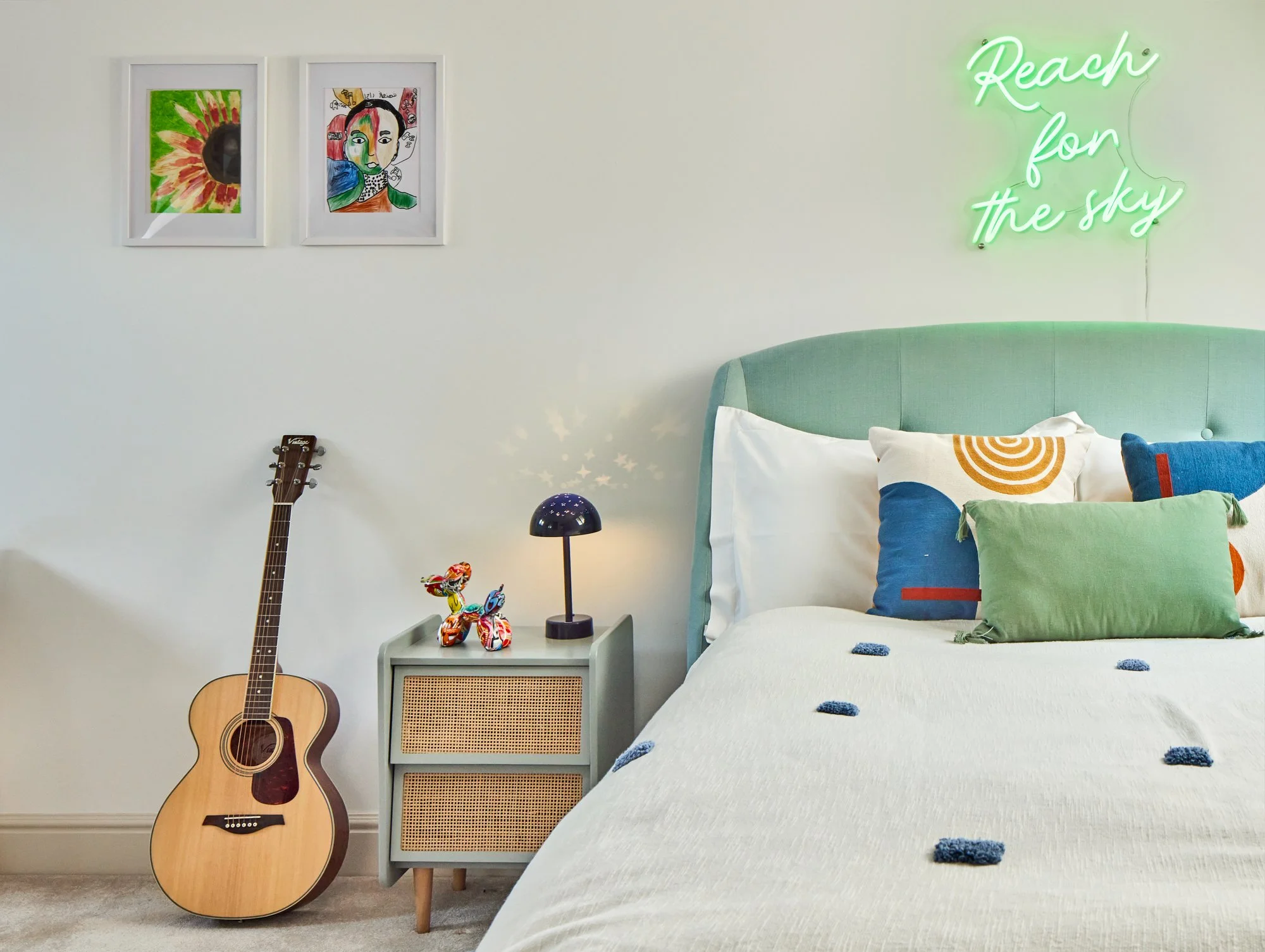 Wimbledon contemporary bedroom with mint green headboard, colorful cushions, wall art, and neon sign.
