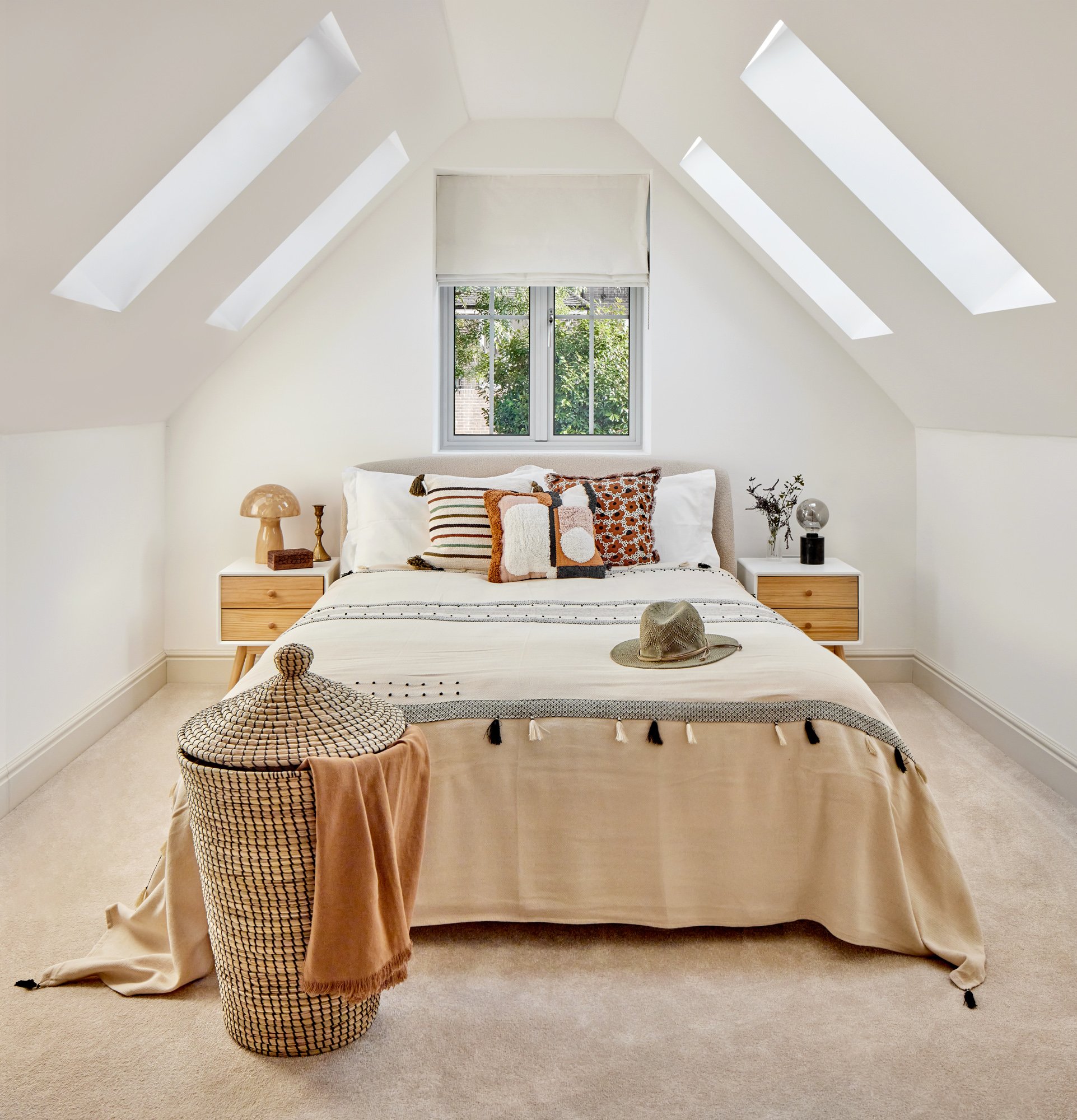 Boho-scandi attic bedroom with skylights, patterned cushions and woven storage basket in our Raynes park project