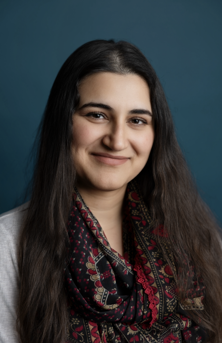 Portrait of a young woman with long dark hair, smiling, wearing a patterned scarf, against a teal background.